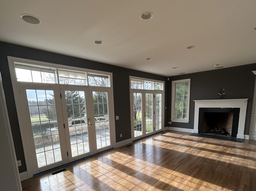 Interior of a home's living room with floor to ceiling glass windows, hardwood flooring, fireplace and blue walls