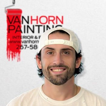 A man wearing a baseball cap is smiling in front of a van horn painting logo