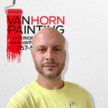 A bald man is standing in front of a van horn painting logo