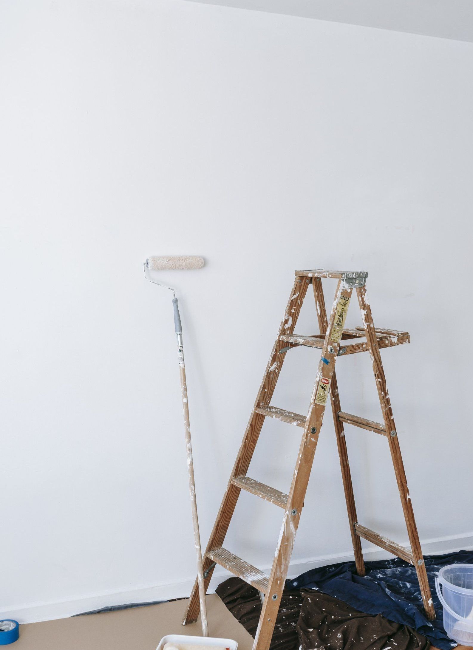 A wooden ladder is sitting next to a paint roller in a room.