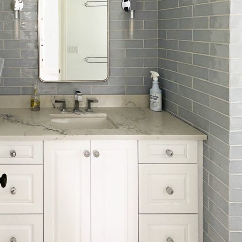 A bathroom with white cabinets , a sink , a mirror and a spray bottle.