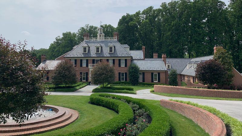 A large brick house with a fountain in front of it surrounded by trees.