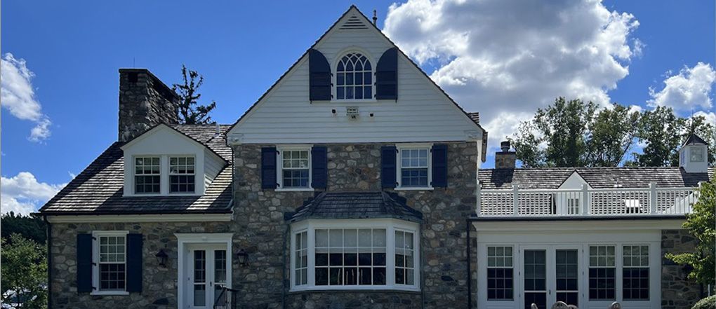 A large stone house with white siding and black shutters on a sunny day.