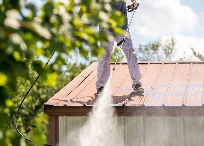 A man is cleaning the roof of a building with a high-pressure washer.