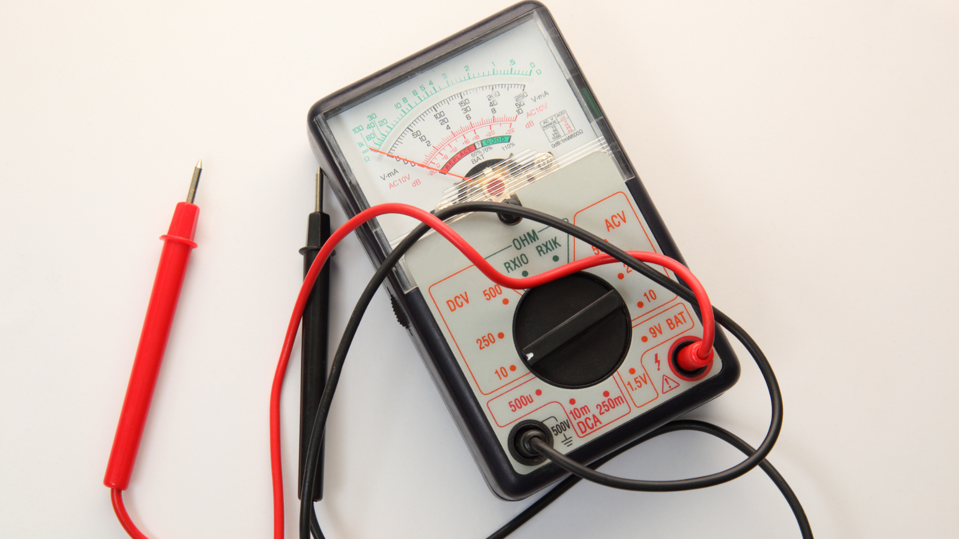 A multimeter is sitting on a white surface next to a red pen.