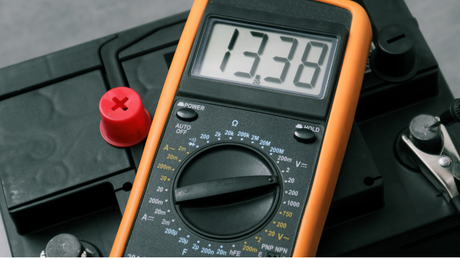 A digital multimeter is sitting on top of a battery