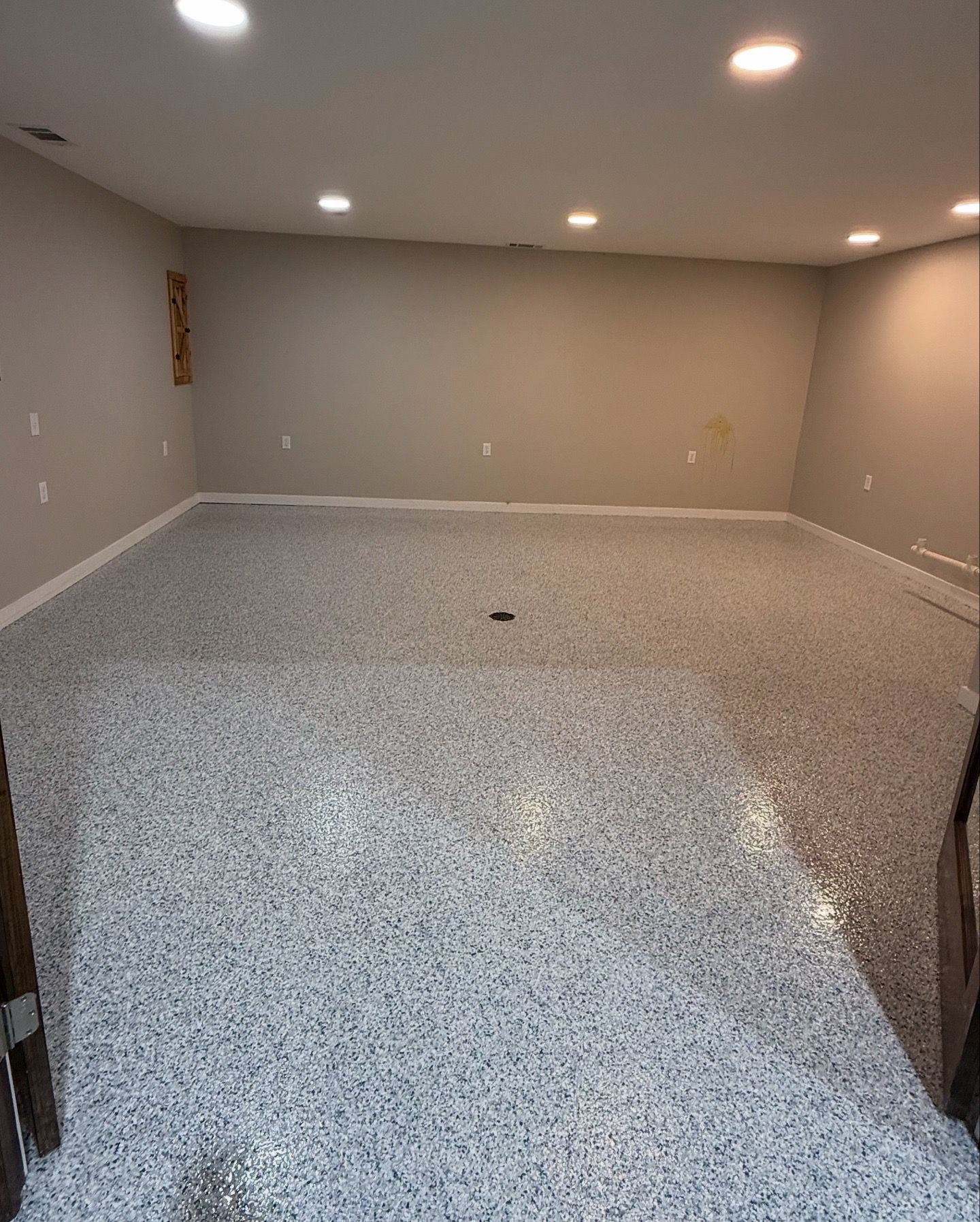 Empty gray basement room with recessed lights and speckled epoxy floor