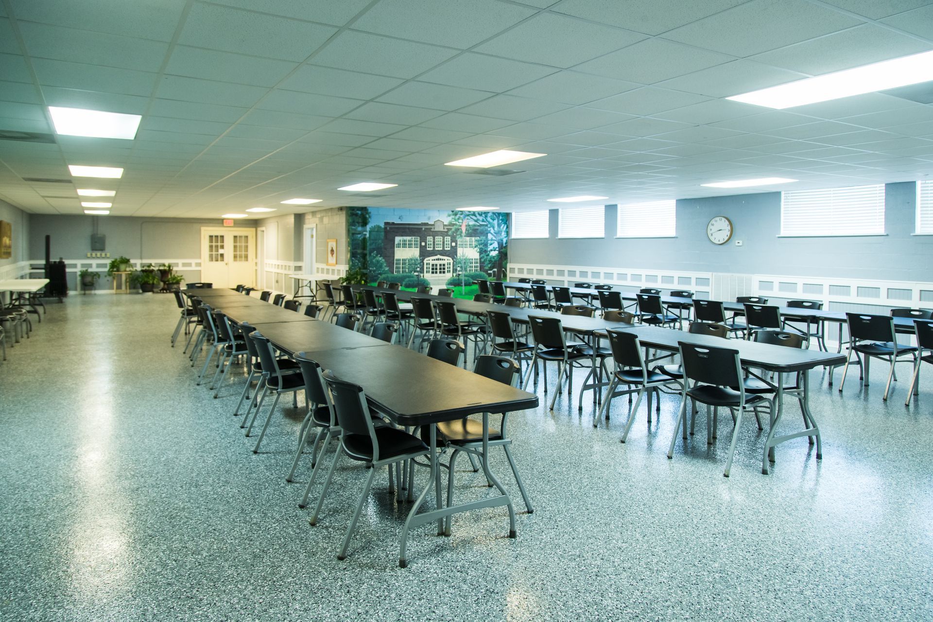 Empty cafeteria with rows of tables and chairs in a bright, fluorescent-lit room