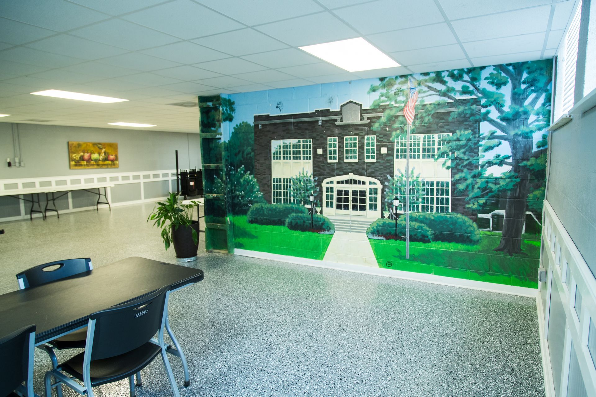 Office lobby with conference table, tiled floor, and large mural of a brick building amid greenery