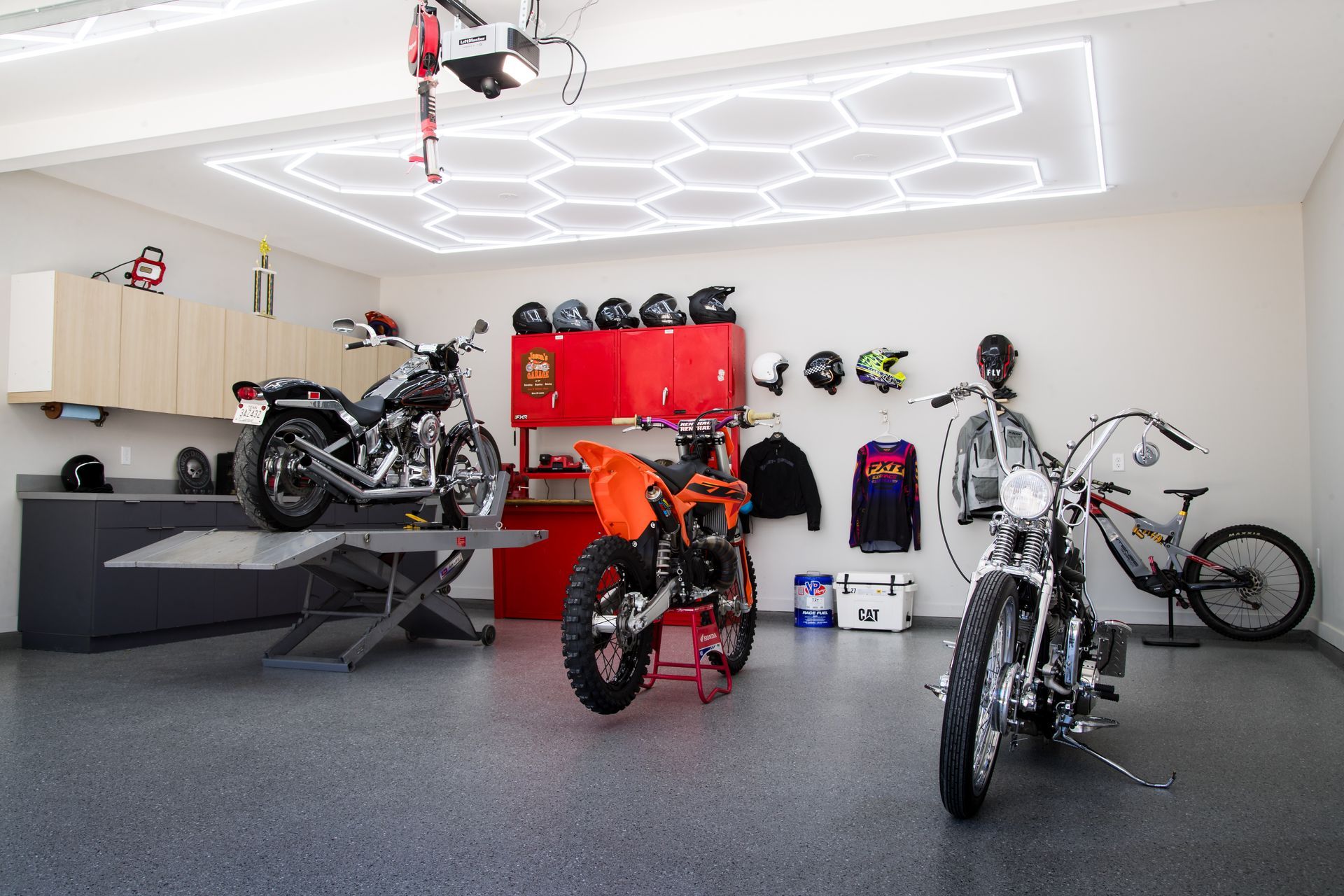 Motorcycle-filled garage with red cabinets, black workbench, and bright hexagon ceiling lights