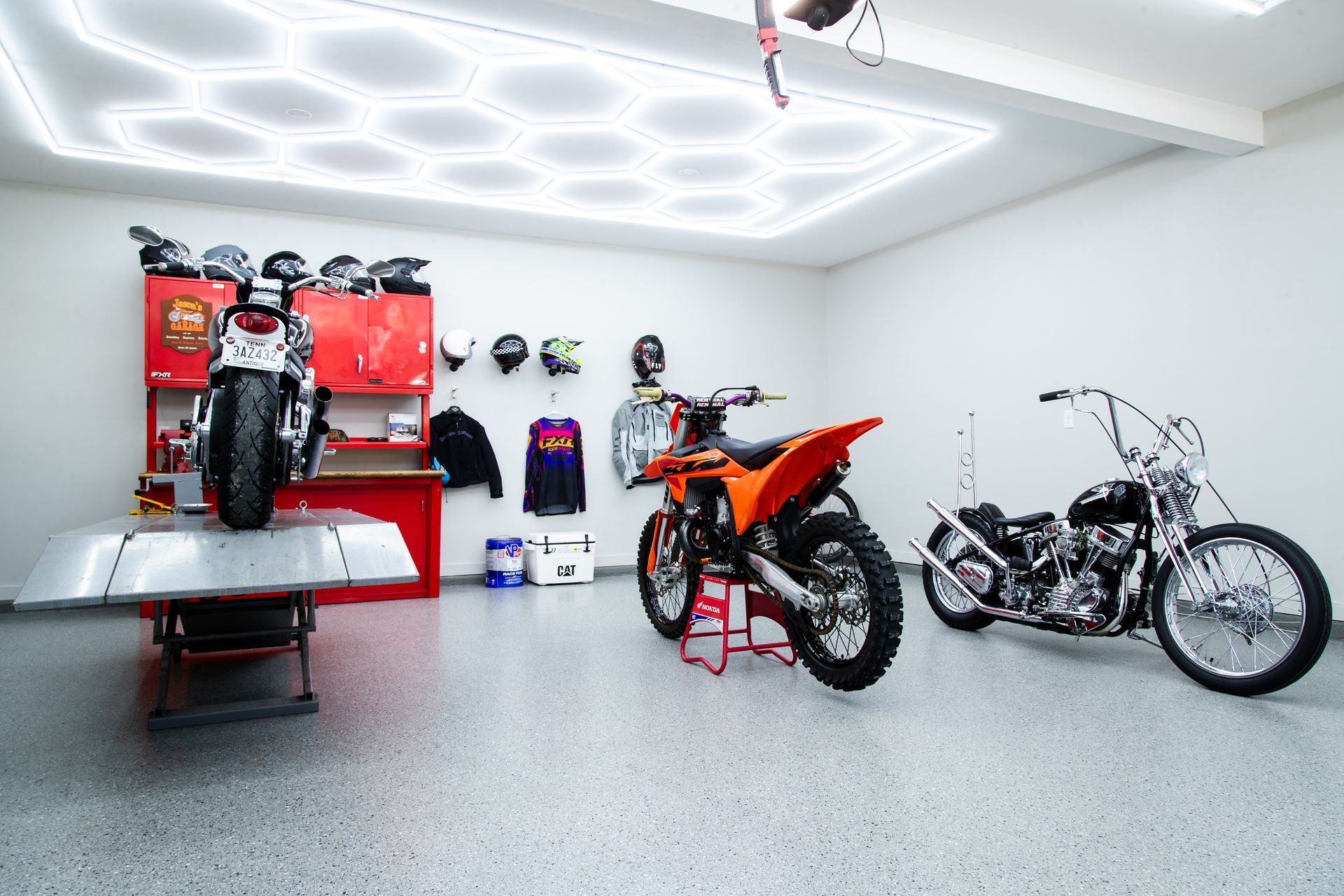 Motorcycles in a bright white garage with hexagon ceiling lights and red storage cabinets