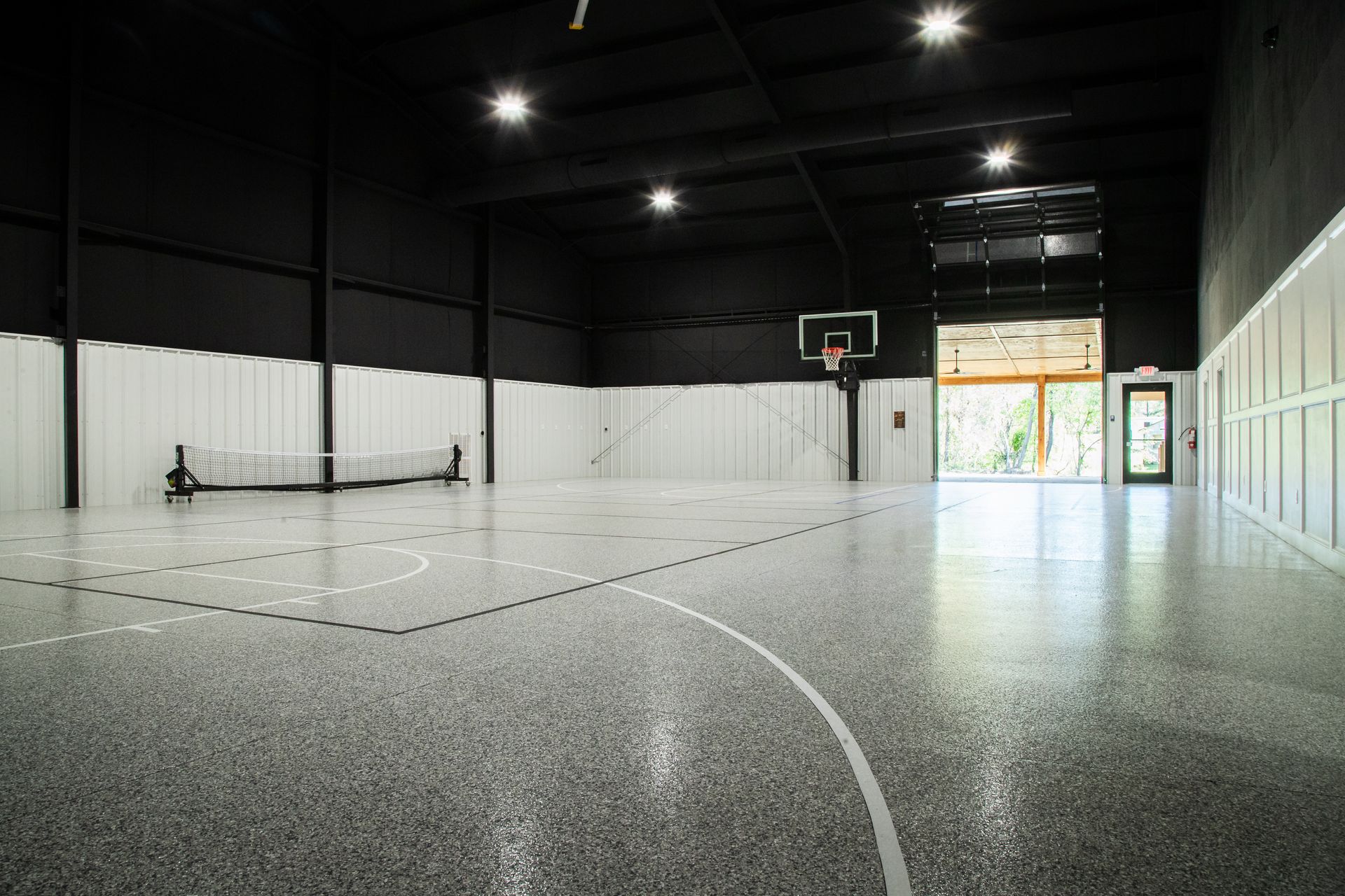 Empty indoor basketball court with white walls, black ceiling, and hoops at both ends.