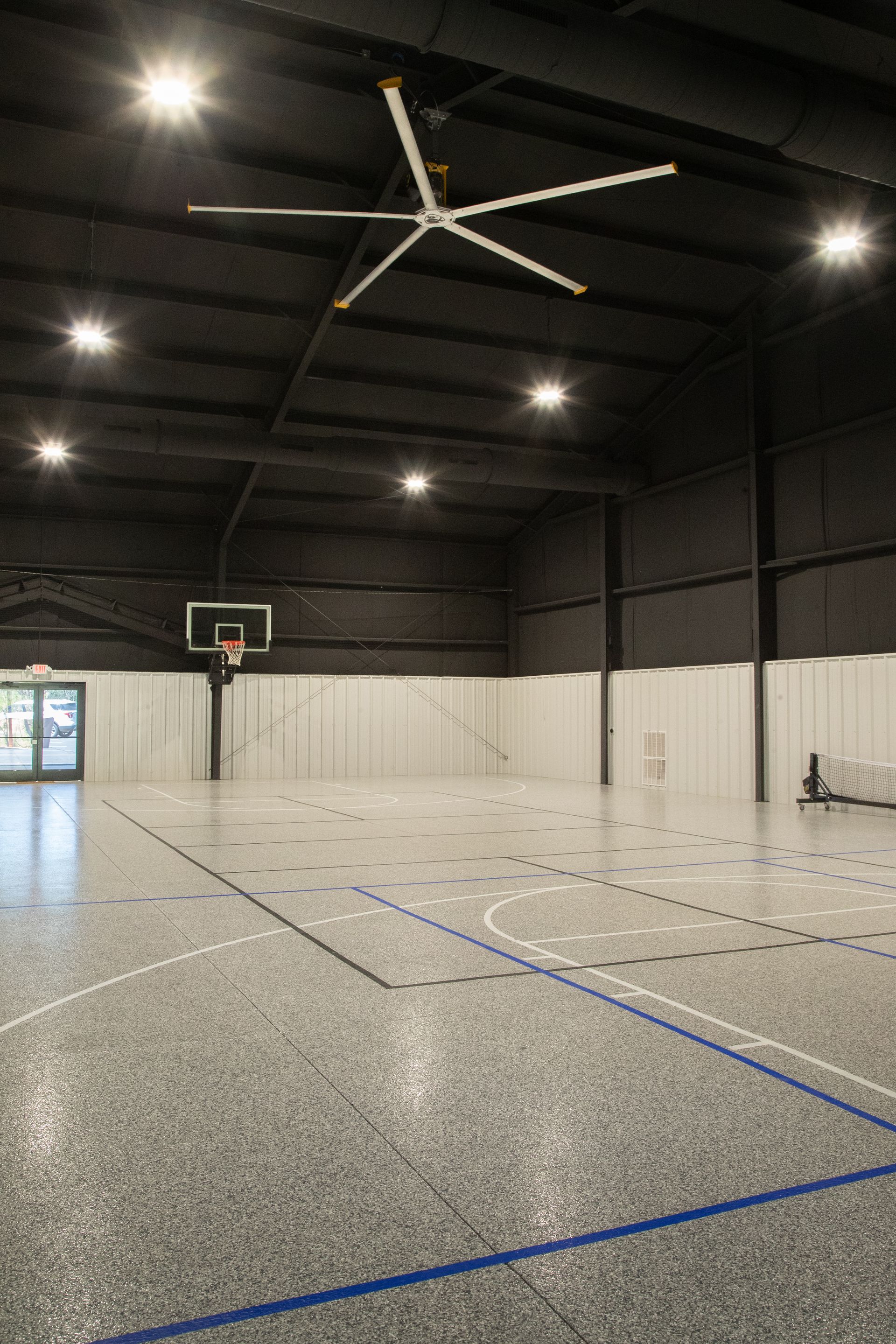 Empty indoor basketball court with high ceilings, a hoop, and blue court lines under bright overhead lights