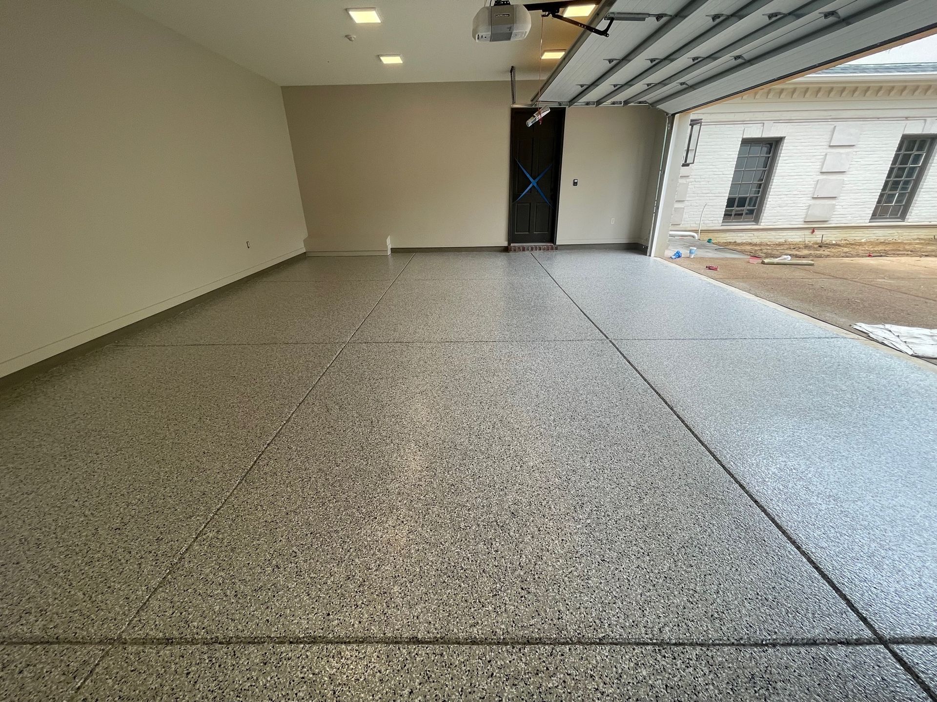 A garage with a gray floor and a garage door open.
