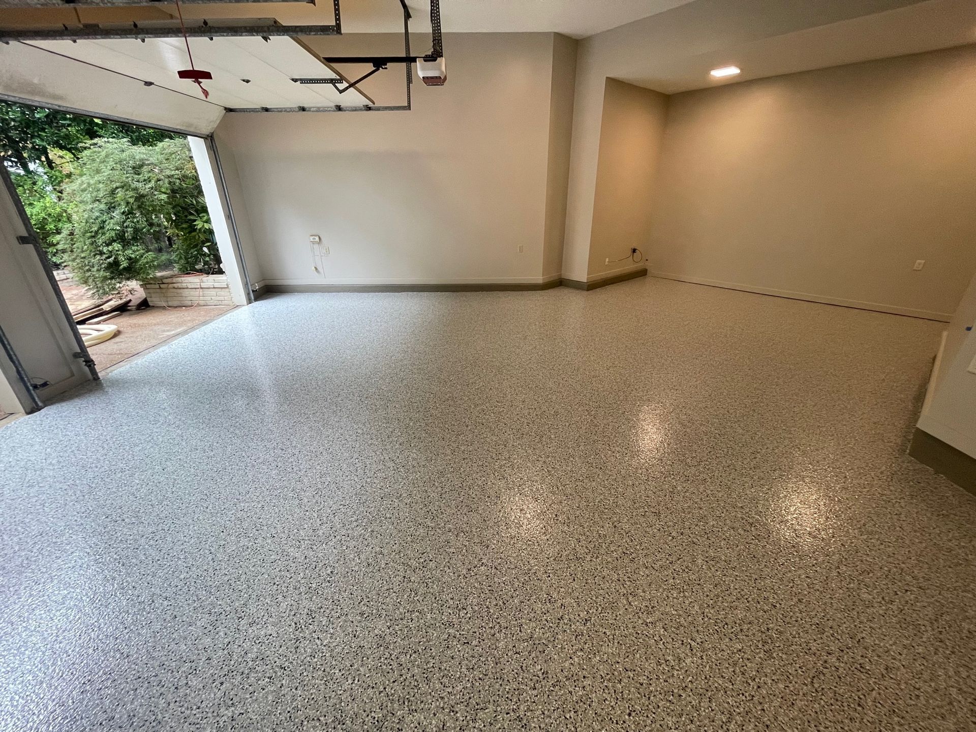 An empty garage with a white floor and a garage door open.