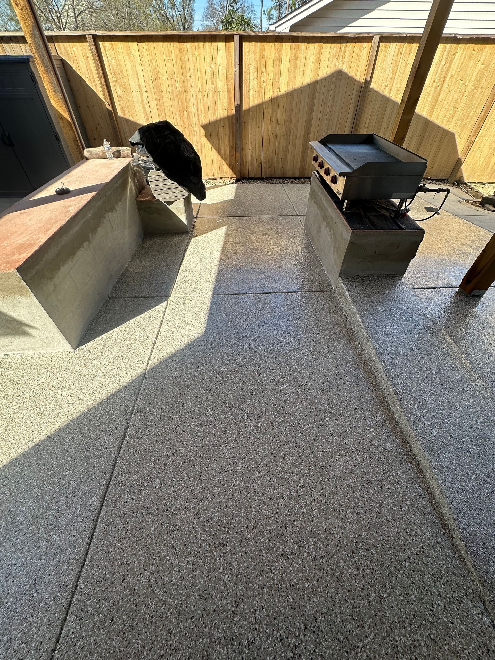 A grill is sitting on top of a concrete patio next to a wooden fence.