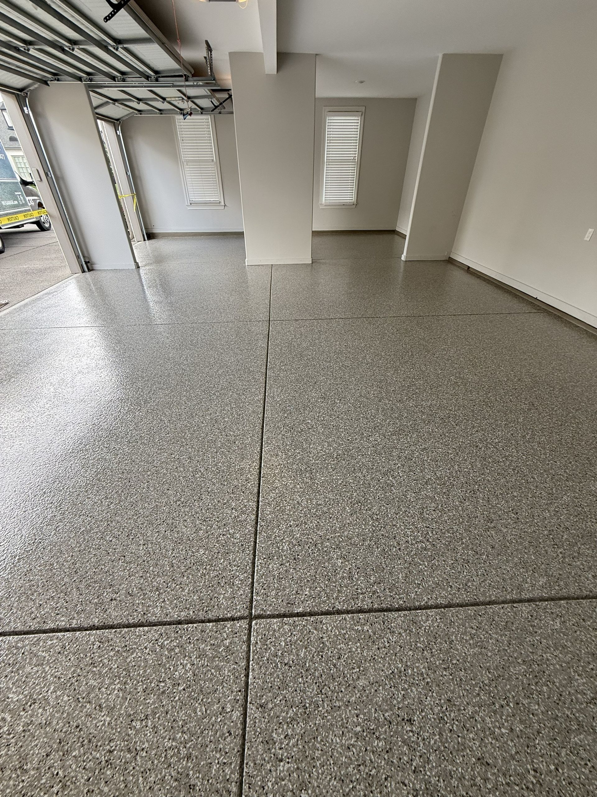 Concrete floor with visible cracks in a commercial interior. Gray and white tones. Open garage door visible.