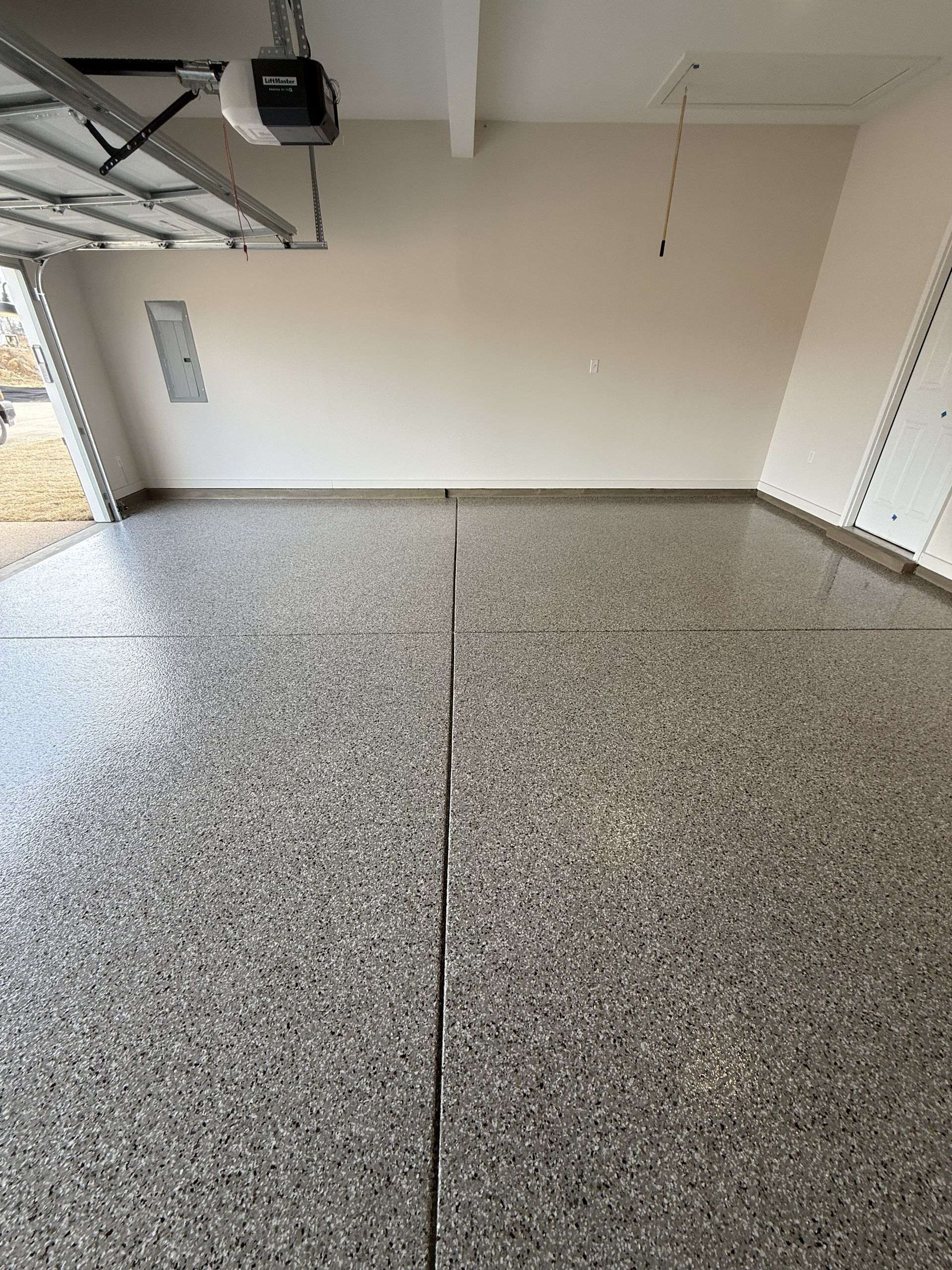 Empty garage with speckled epoxy floor, beige walls, and garage door opener.