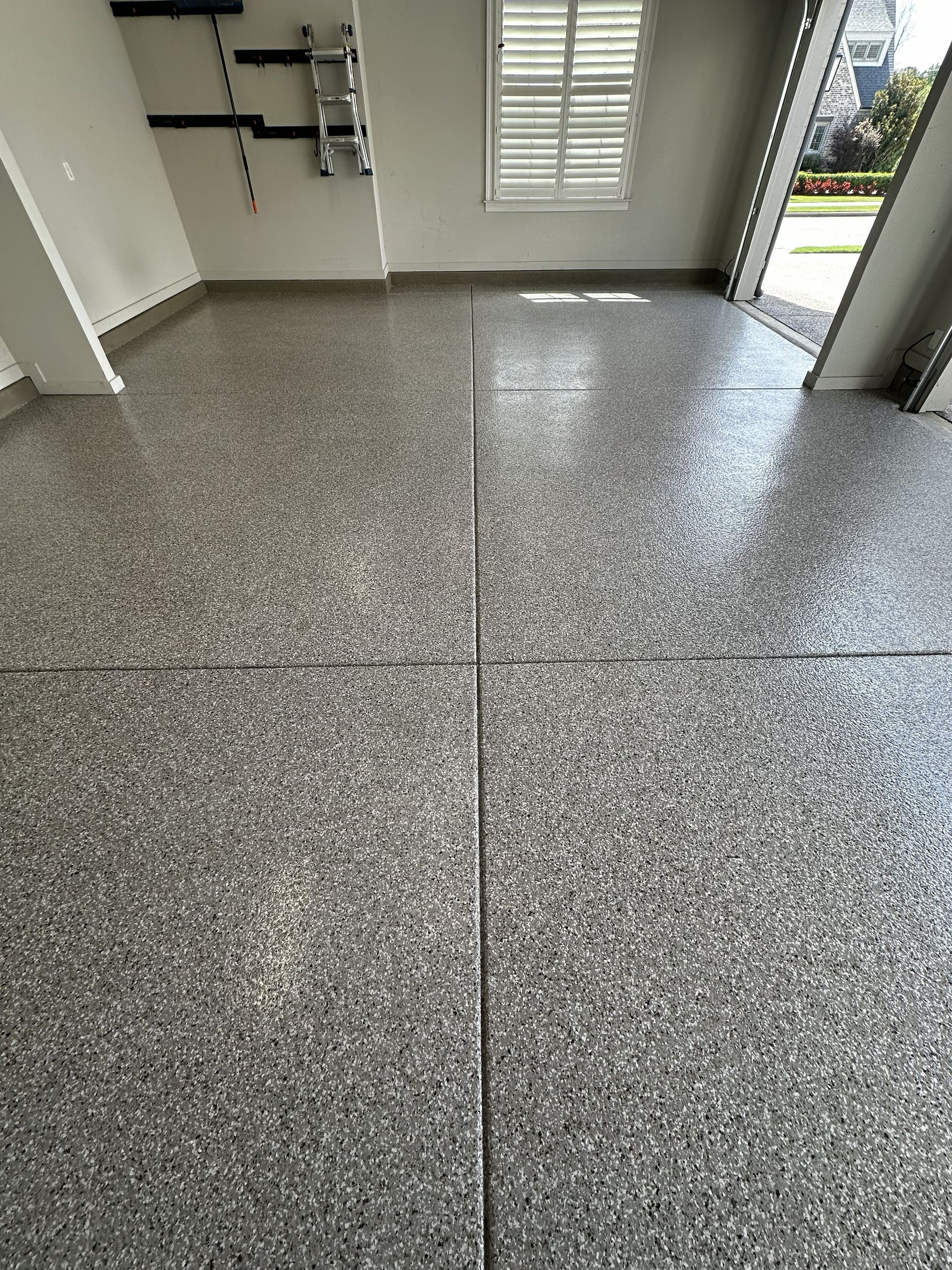 Garage floor with a speckled, glossy finish, gray tones. The garage door is open.