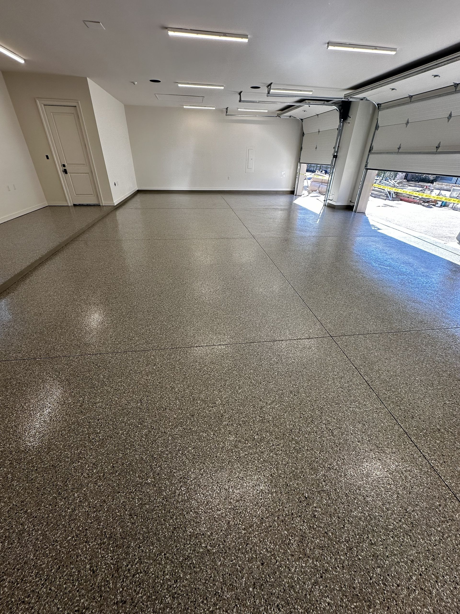 Empty garage with glossy, speckled gray floor; white walls; open garage door.