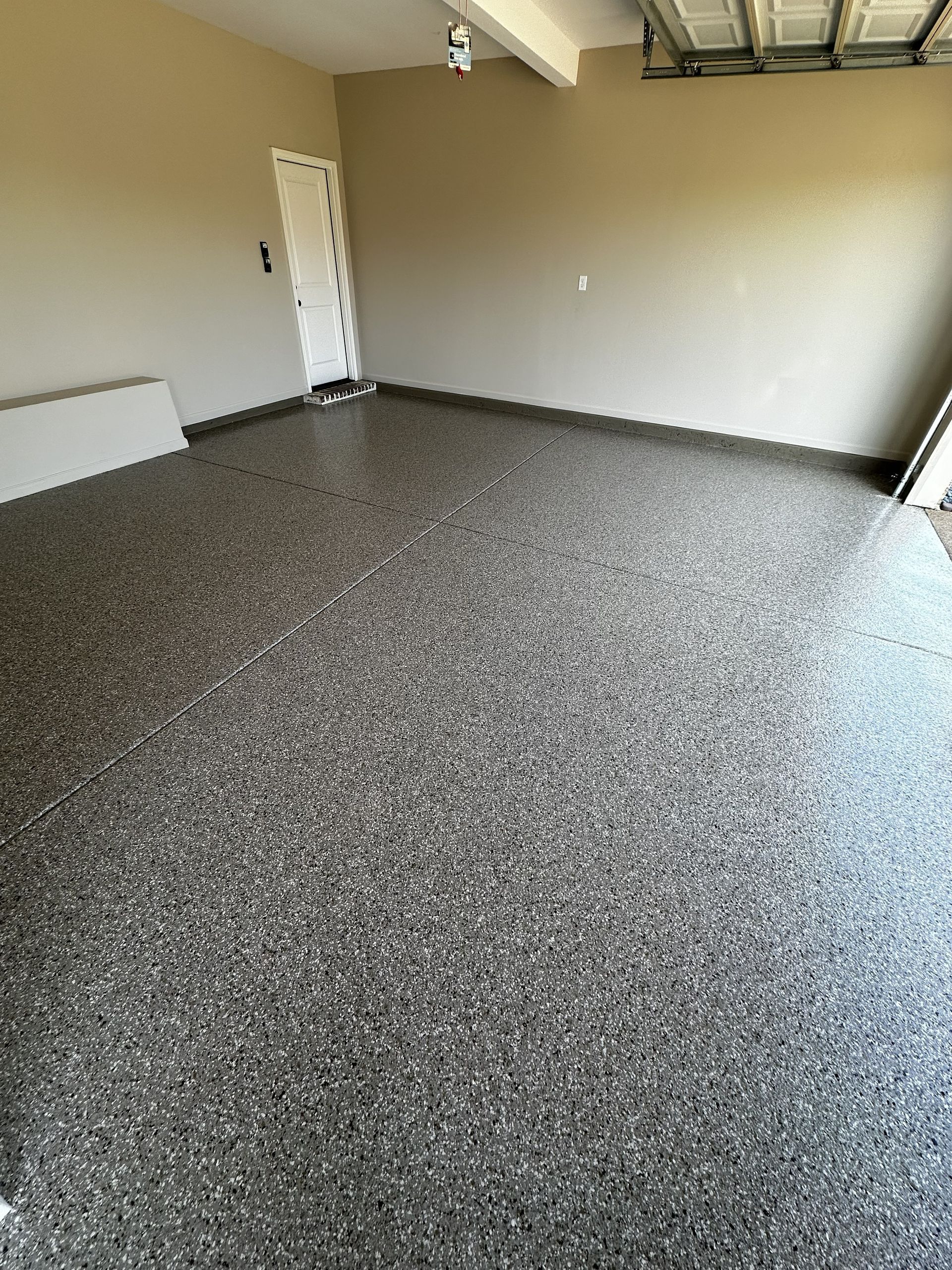 An empty garage with a speckled epoxy floor. Walls are light beige. Garage door is up.