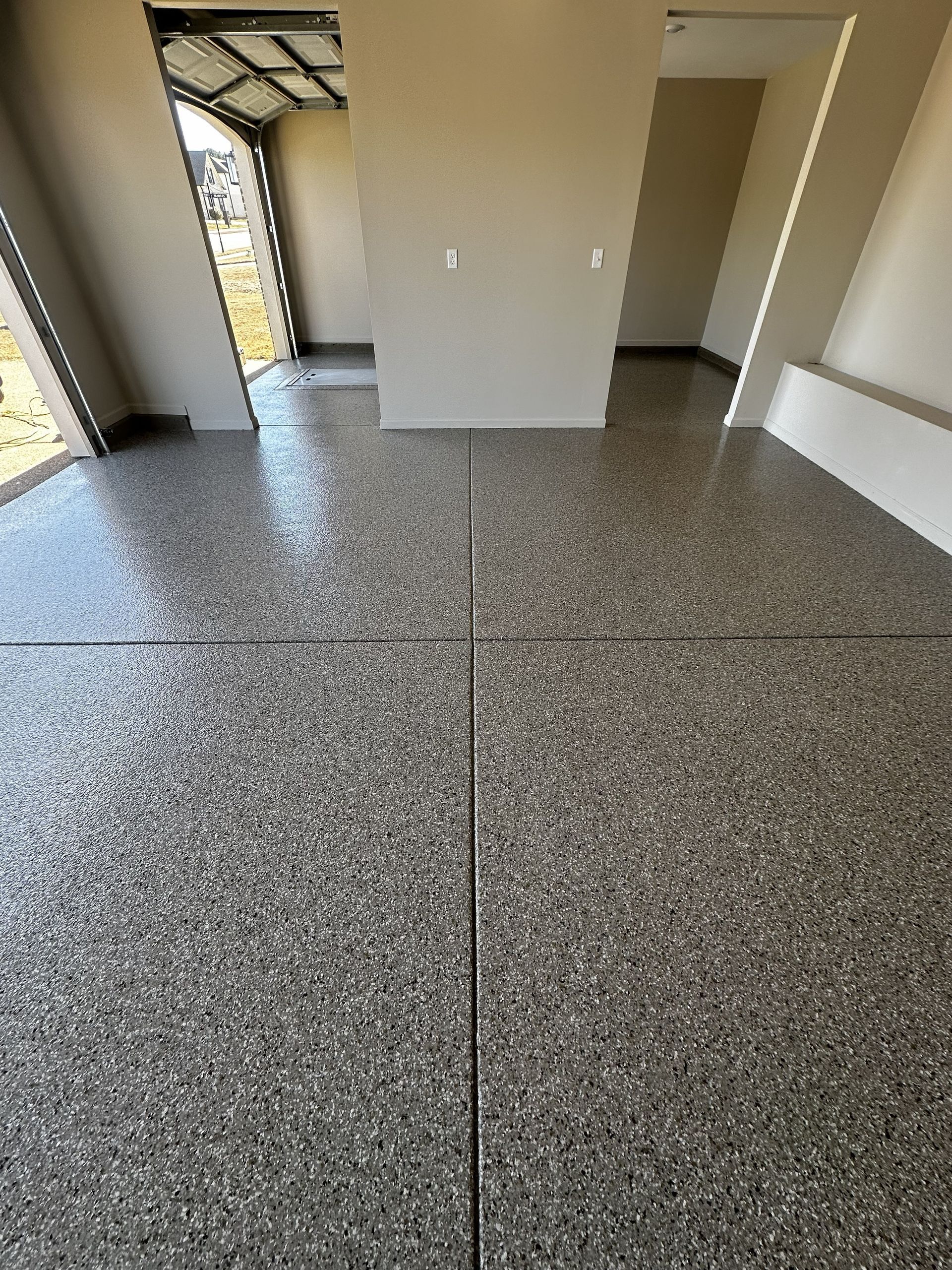 Garage interior with speckled epoxy flooring. Gray, black, and white colors with vertical lines and open garage door.