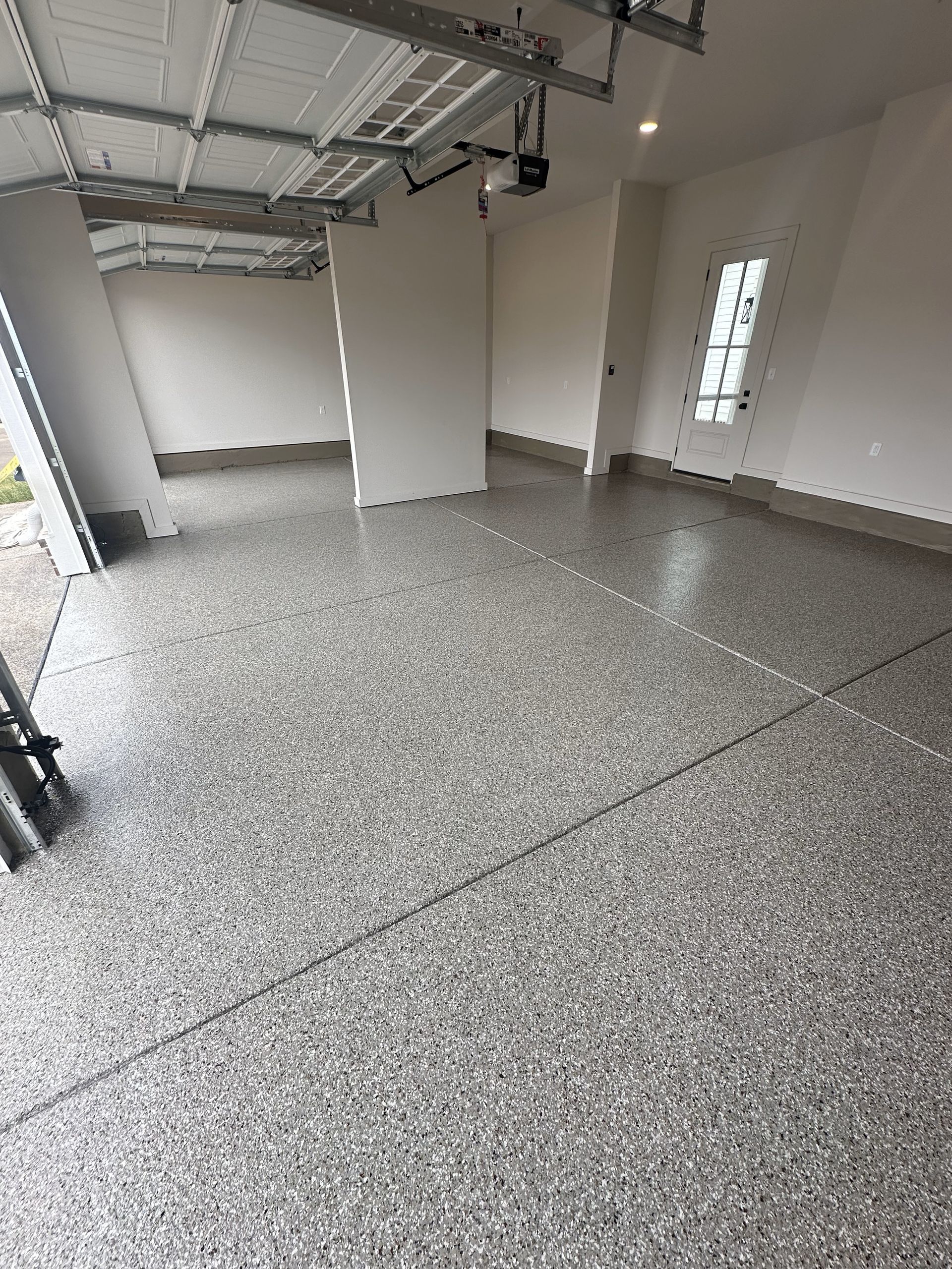 A garage with a concrete floor and a garage door open.