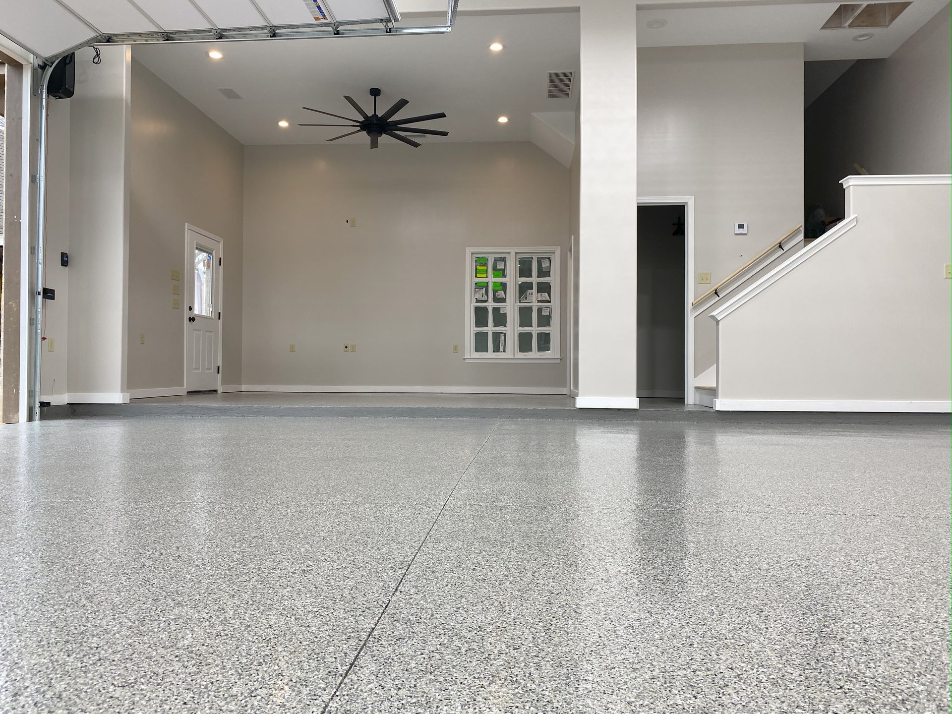 An empty garage with a ceiling fan and stairs