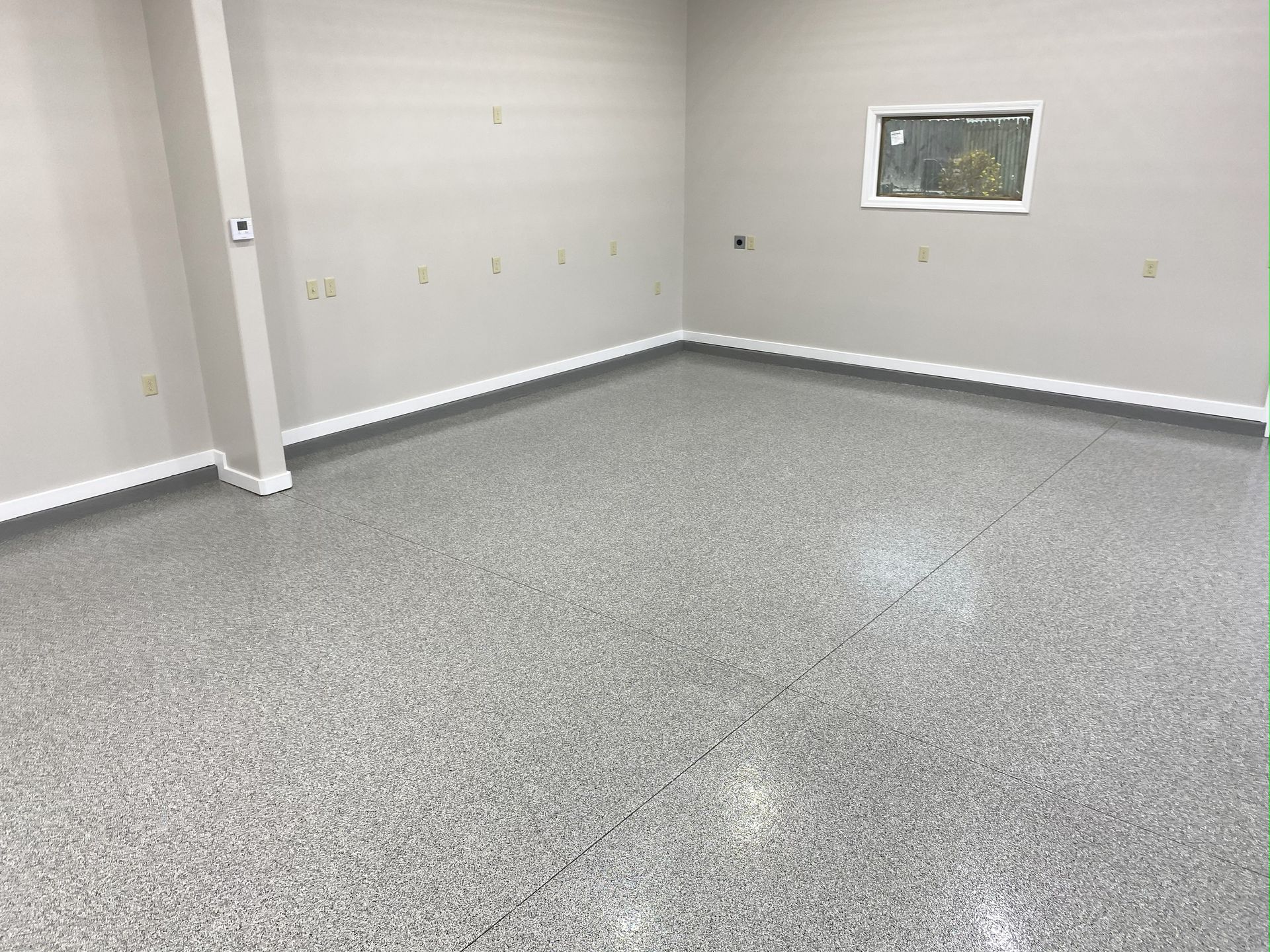 An empty room with a gray floor and a window.