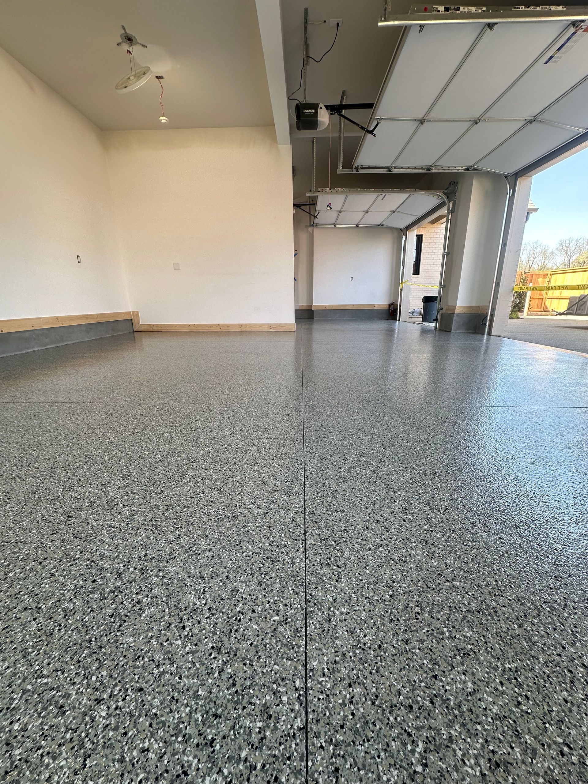 A garage with a gray floor and a garage door open.