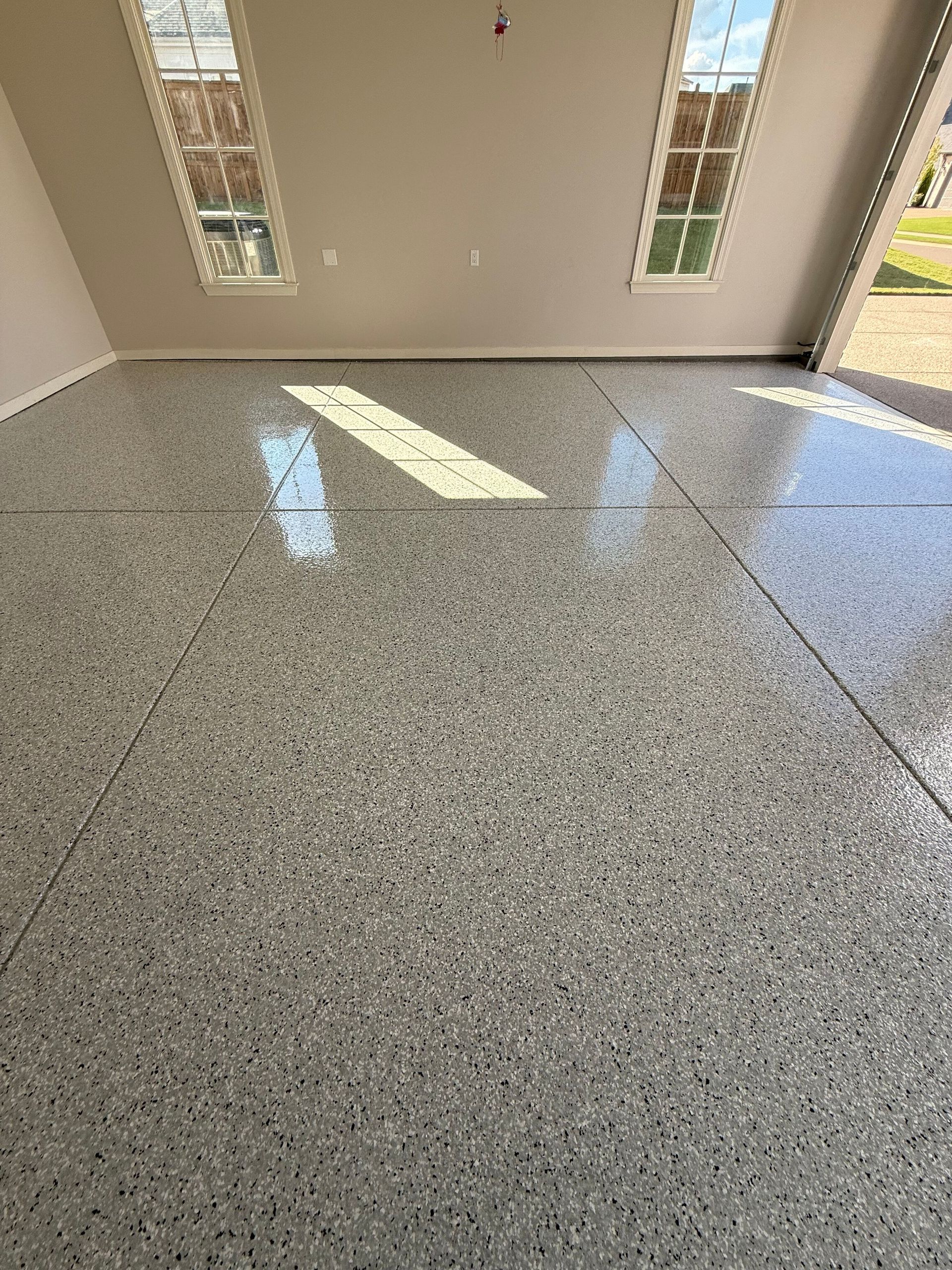 Garage with a speckled gray epoxy floor, two windows, and off-white walls.