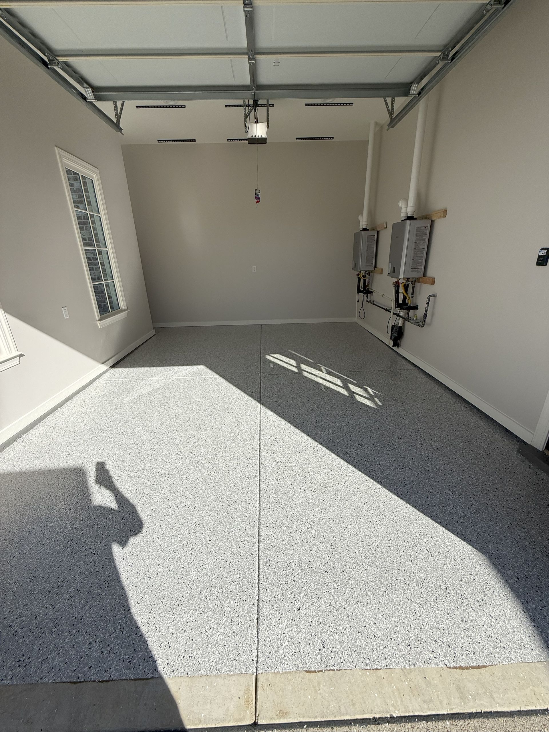 Empty garage with gray speckled epoxy floor and water heaters on the right wall.