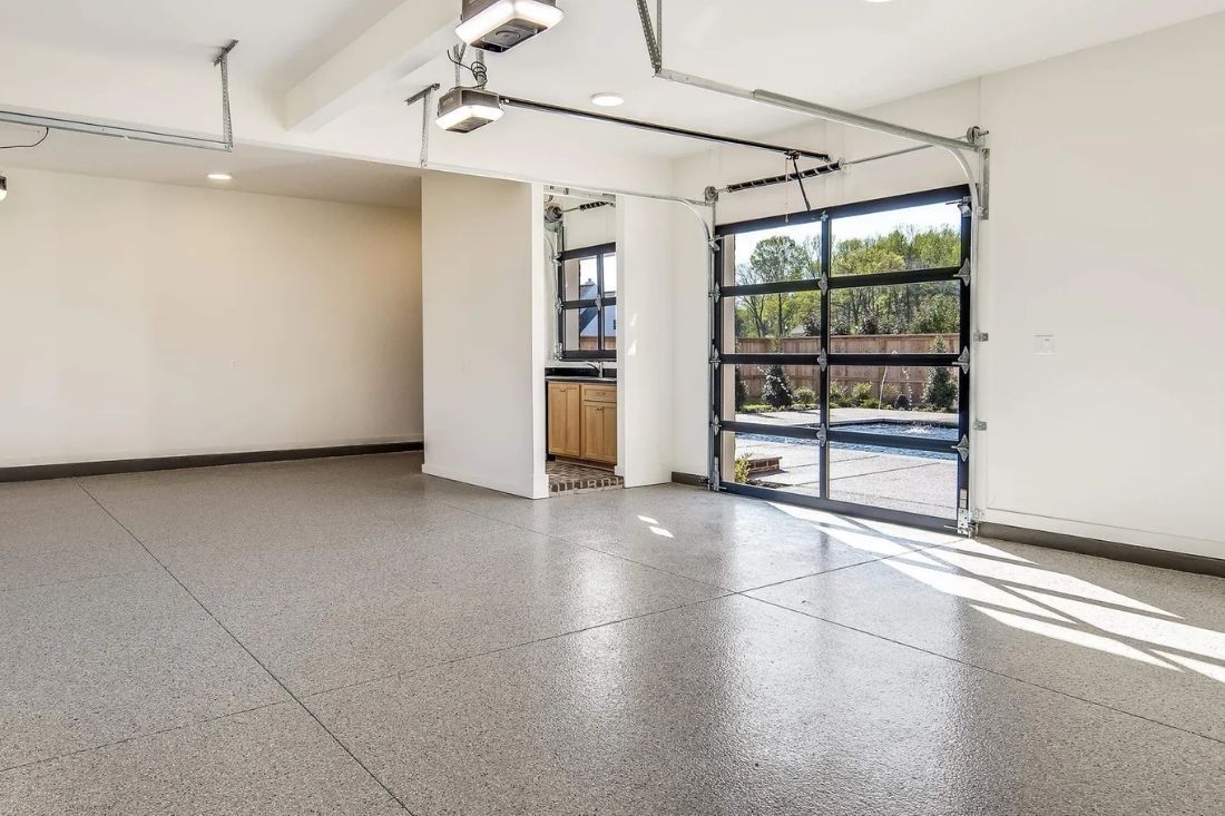 Empty garage with speckled gray floor and glass door.