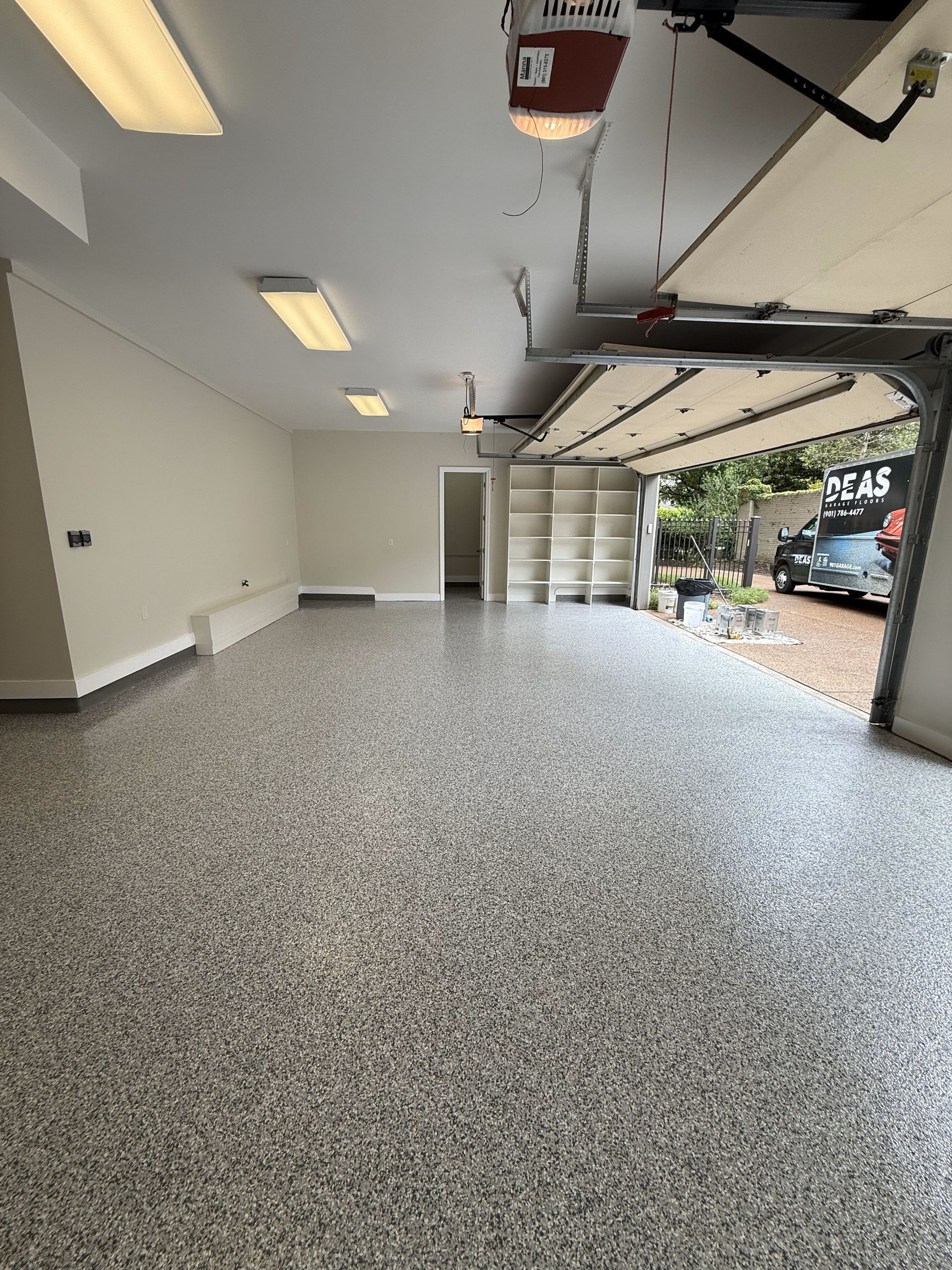 An empty garage with a garage door open and a car parked in the driveway.