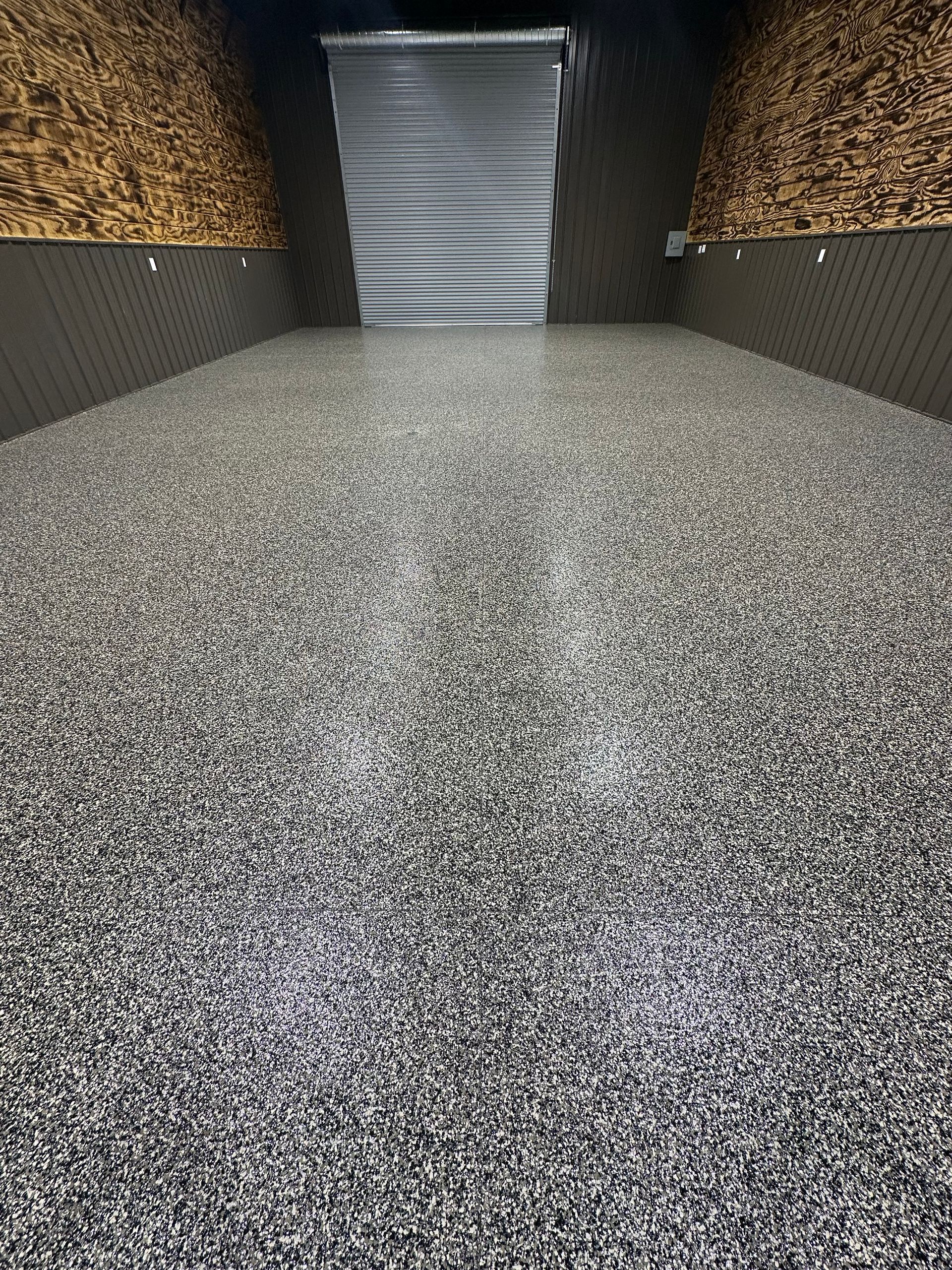 Epoxy floor with speckled aggregate in a long, dark room with wooden wall panels.