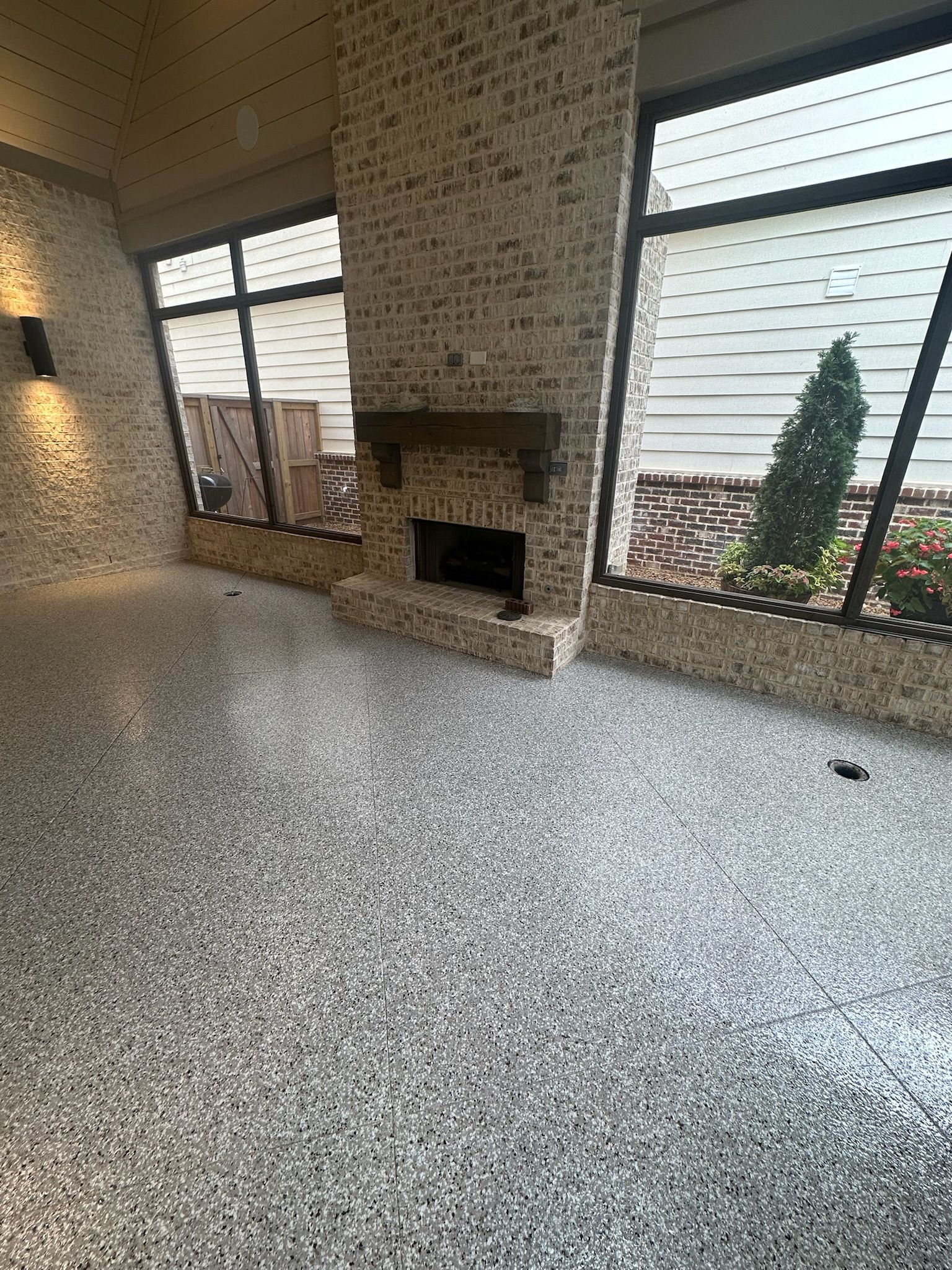 Spacious carpeted living room with brick fireplace and large windows overlooking a fenced yard