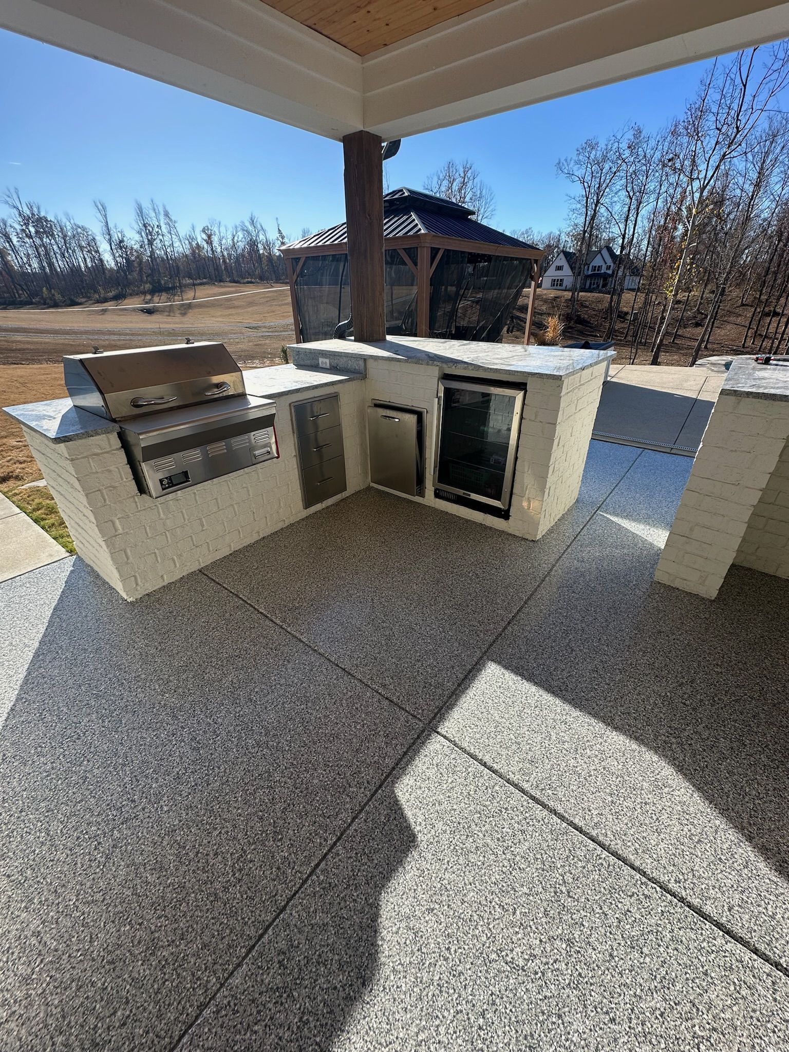 Outdoor patio with built-in stone grill and countertop under a covered roof, overlooking a yard