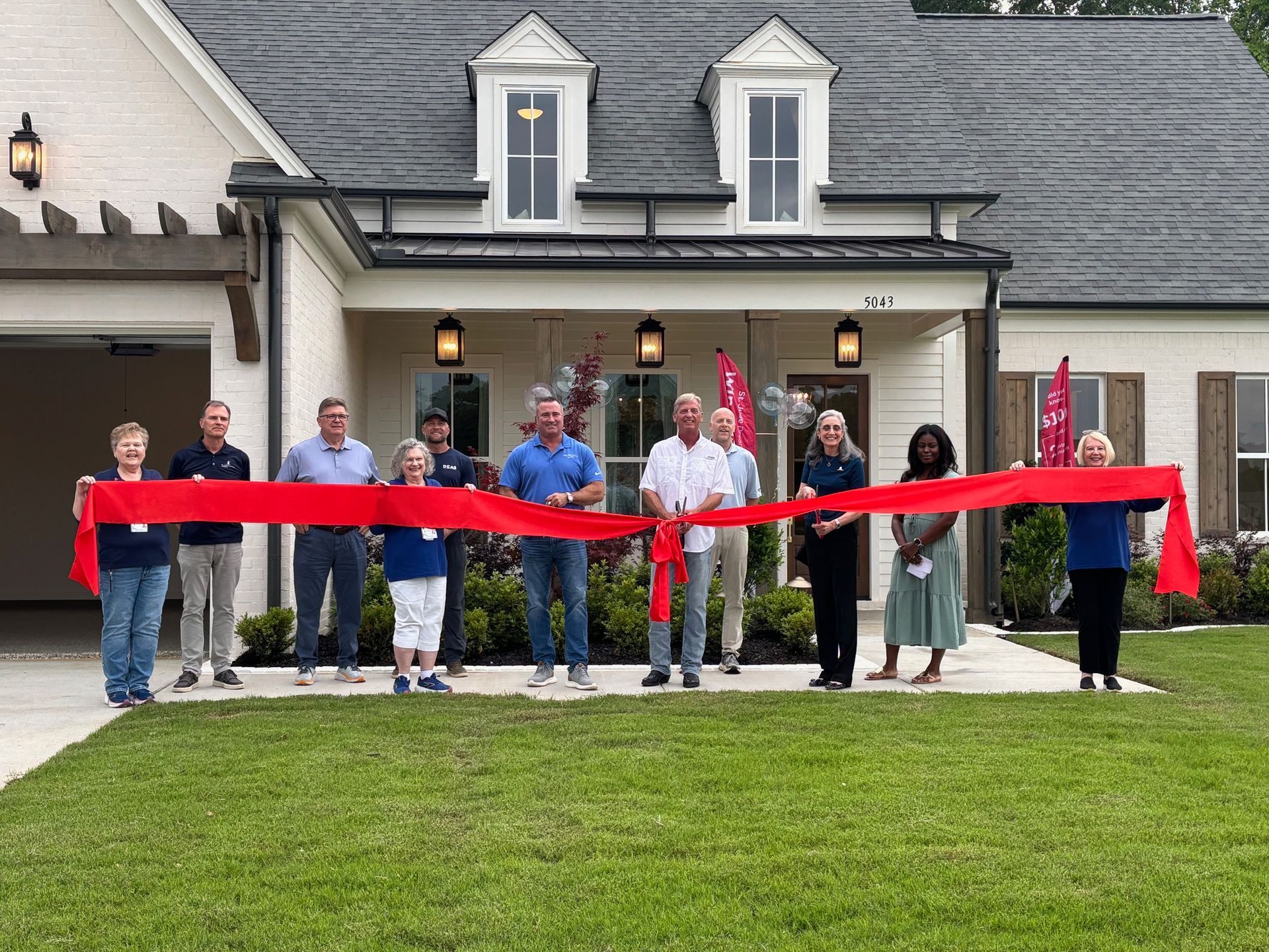 People holding a long red ribbon in front of a building during a ribbon-cutting ceremony