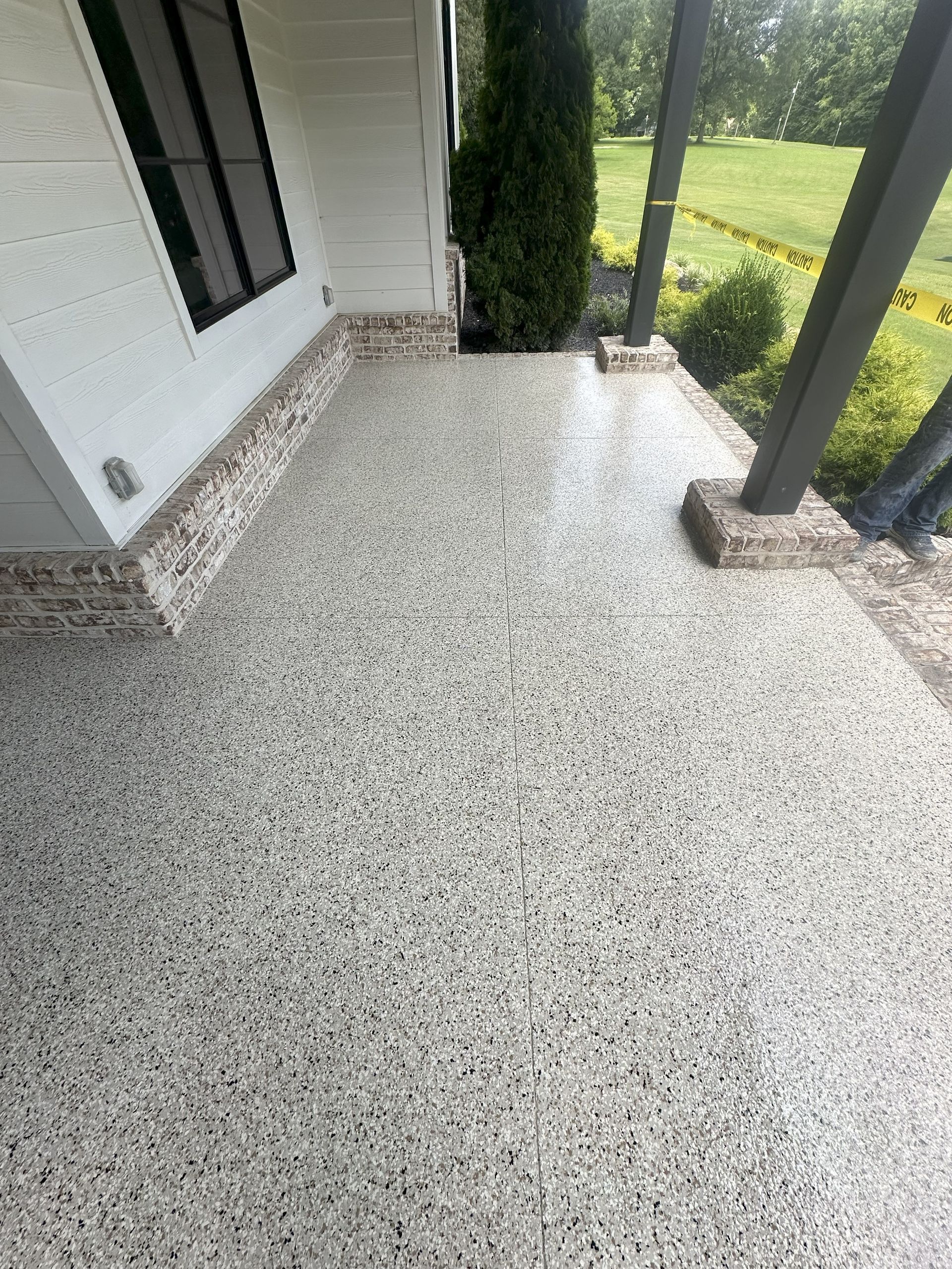 Concrete porch with a speckled gray and white finish, adjacent to a brick wall and a house.