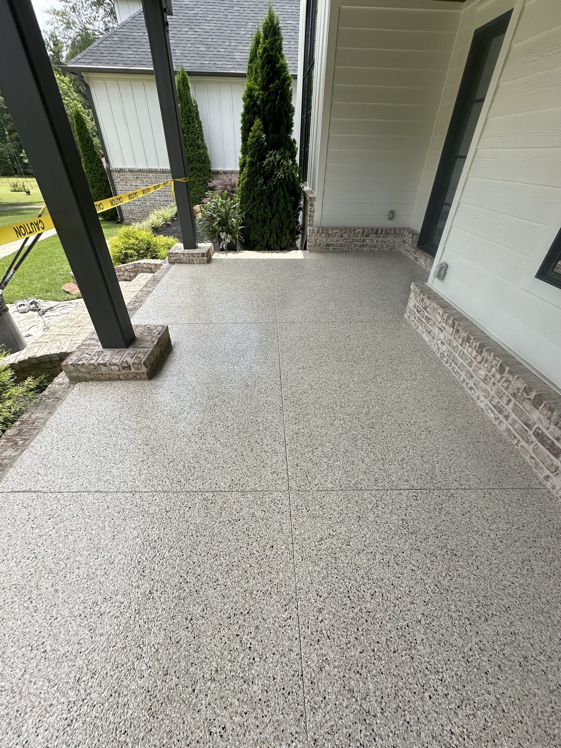 Concrete patio with speckled gray and black aggregate. Brown brick base on wall and support columns.