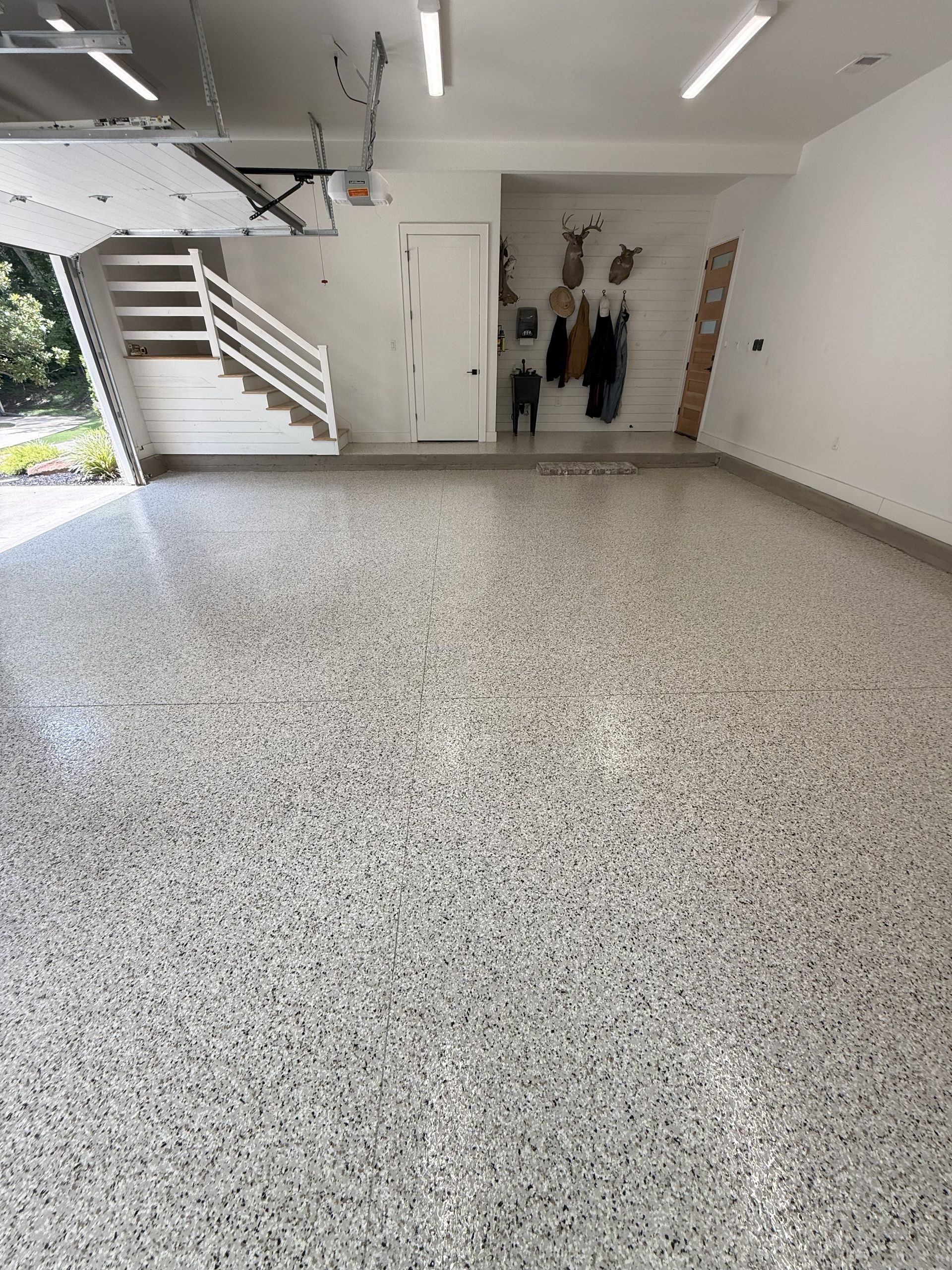 A garage with a speckled epoxy floor, white walls, and a stairway to the left.