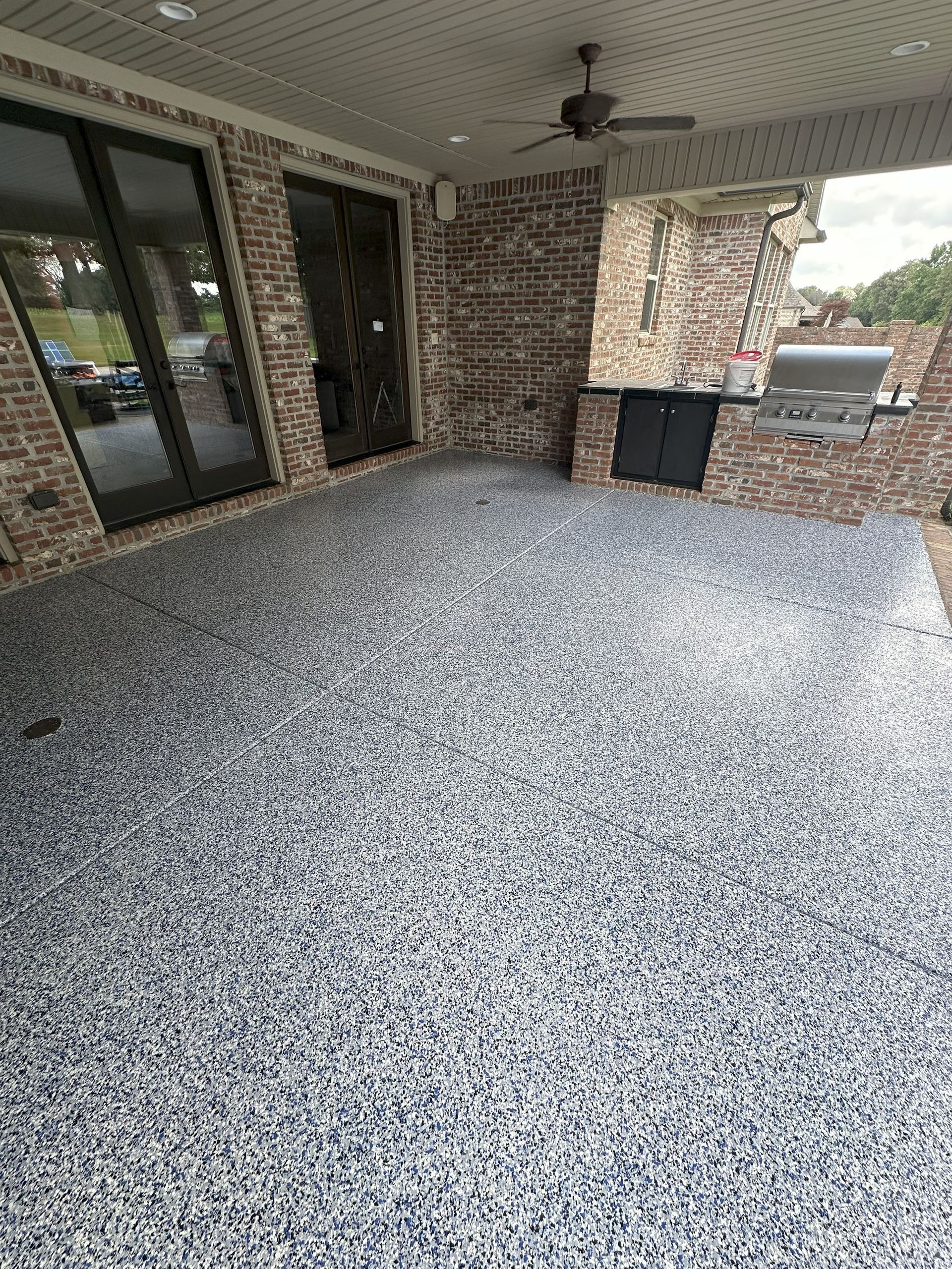 Patio with epoxy flooring, brick walls, grill, and glass doors.