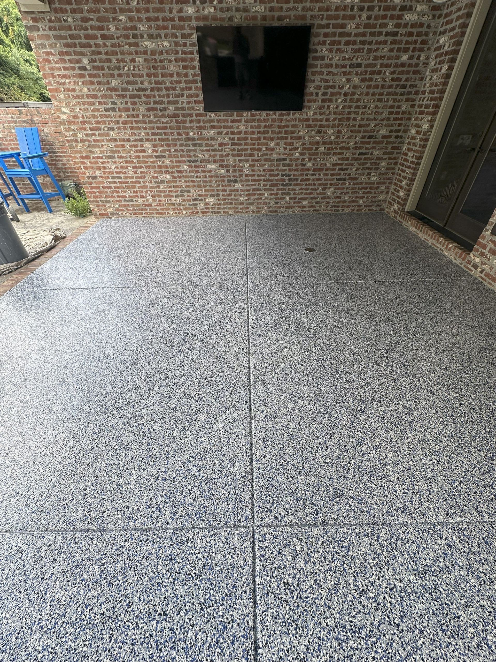 Patio with dark flecked flooring, brick wall, and mounted TV.
