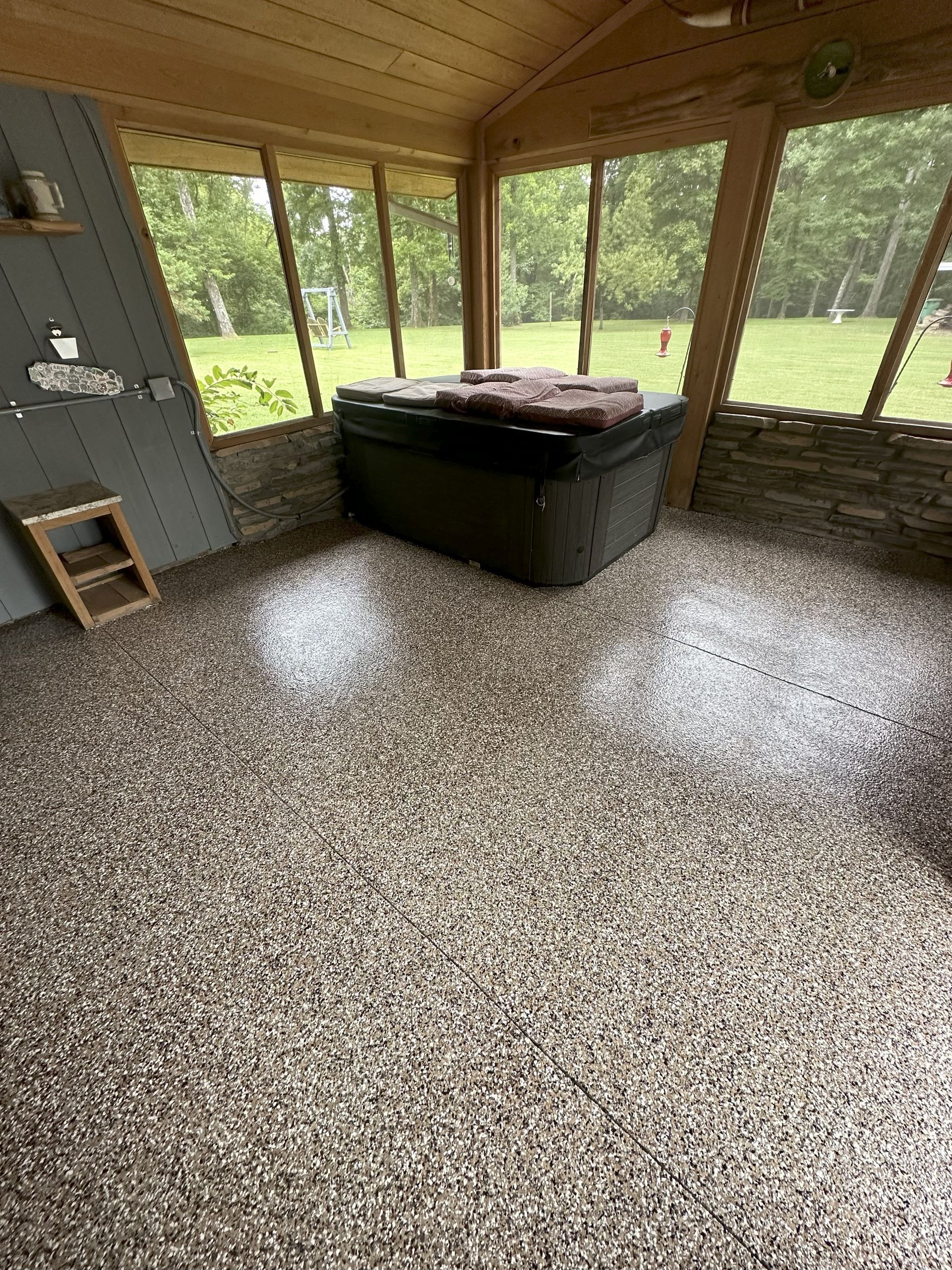 Screened porch with gray speckled flooring, hot tub, wooden trim, and a small stool.