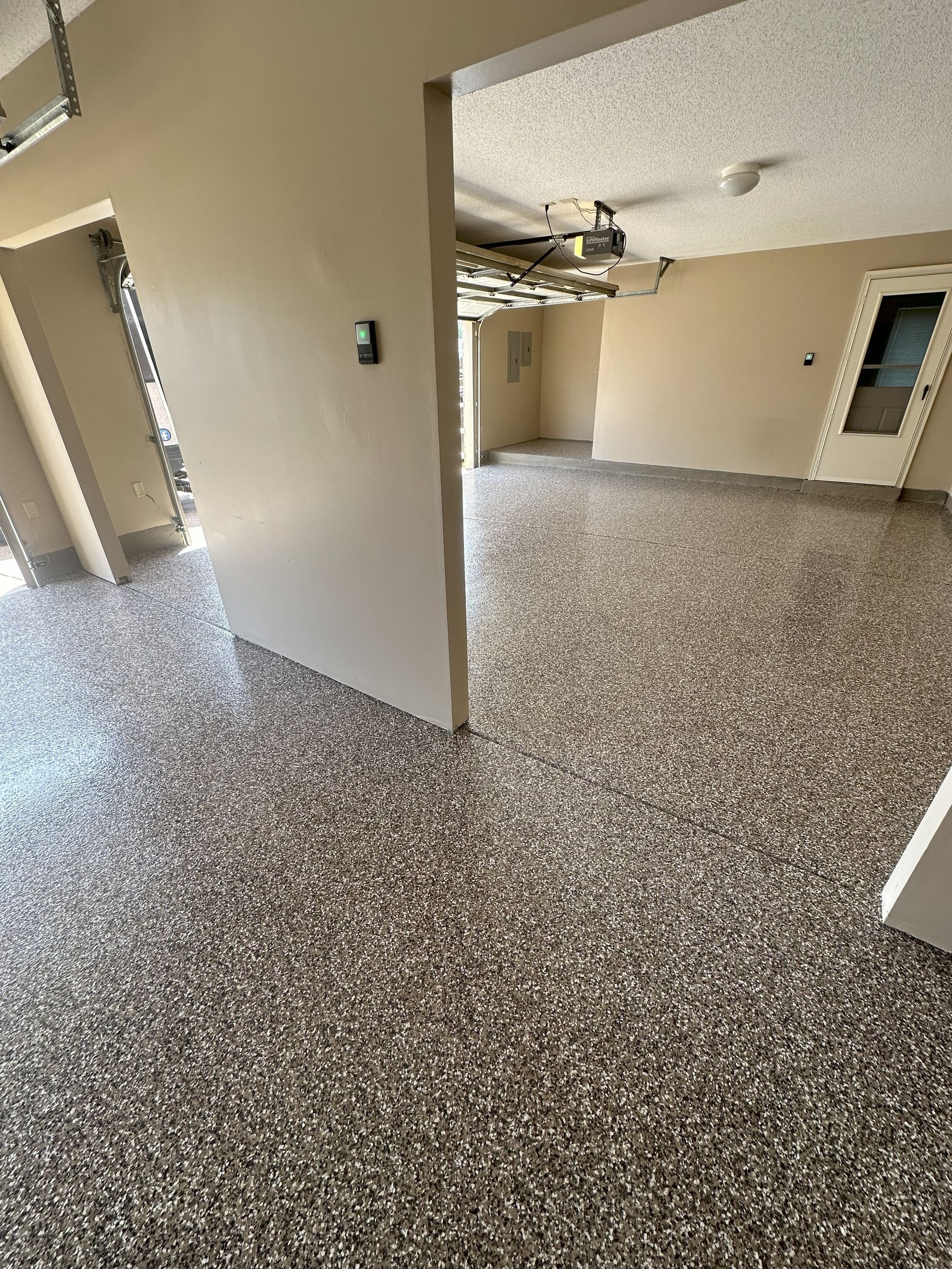 Room with speckled flooring and light-colored walls; open doorway leads to another room; ceiling fan visible.