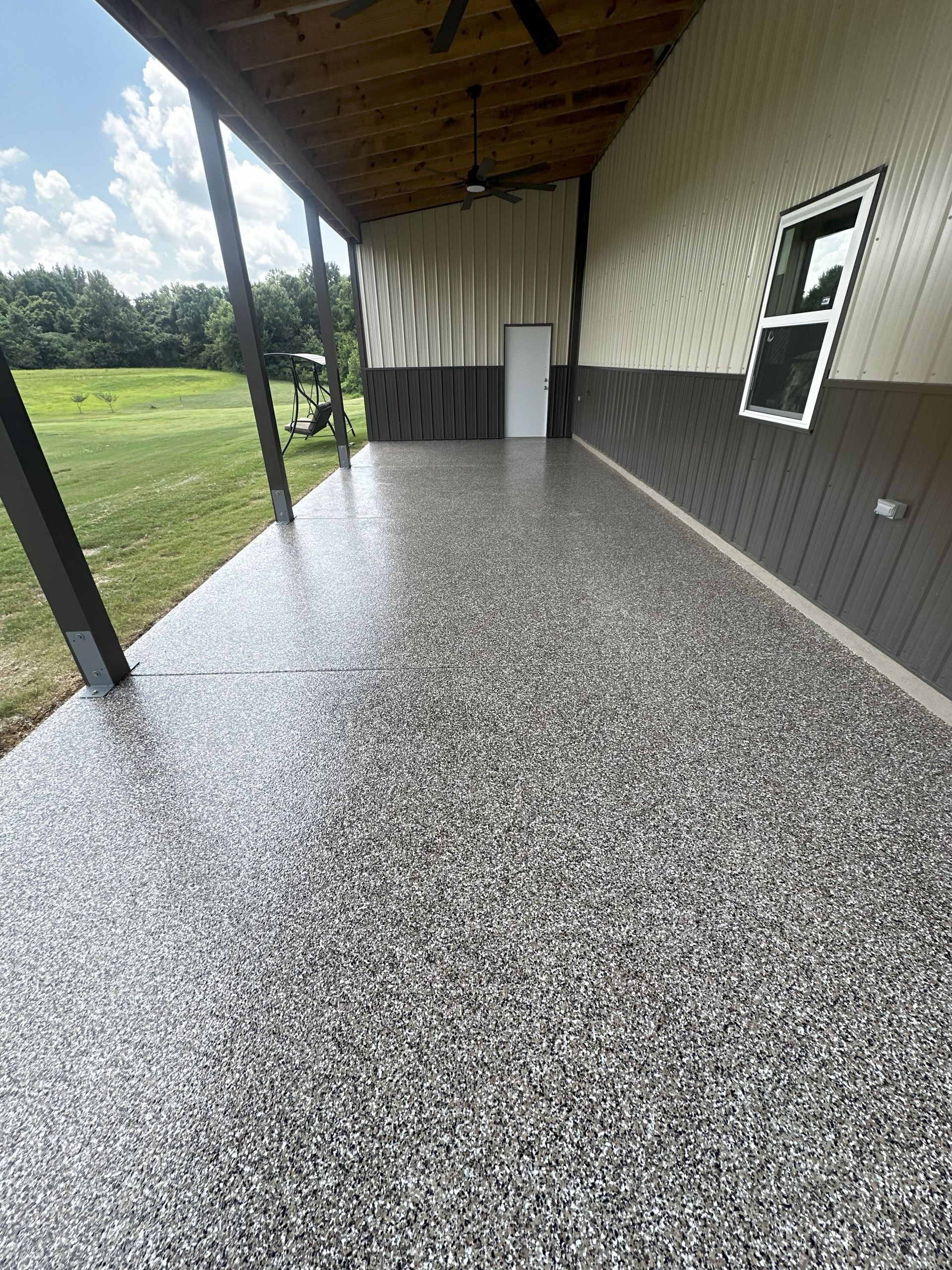 Covered porch with epoxy flooring, brown and white wall, door, and window. Green grass visible in background.