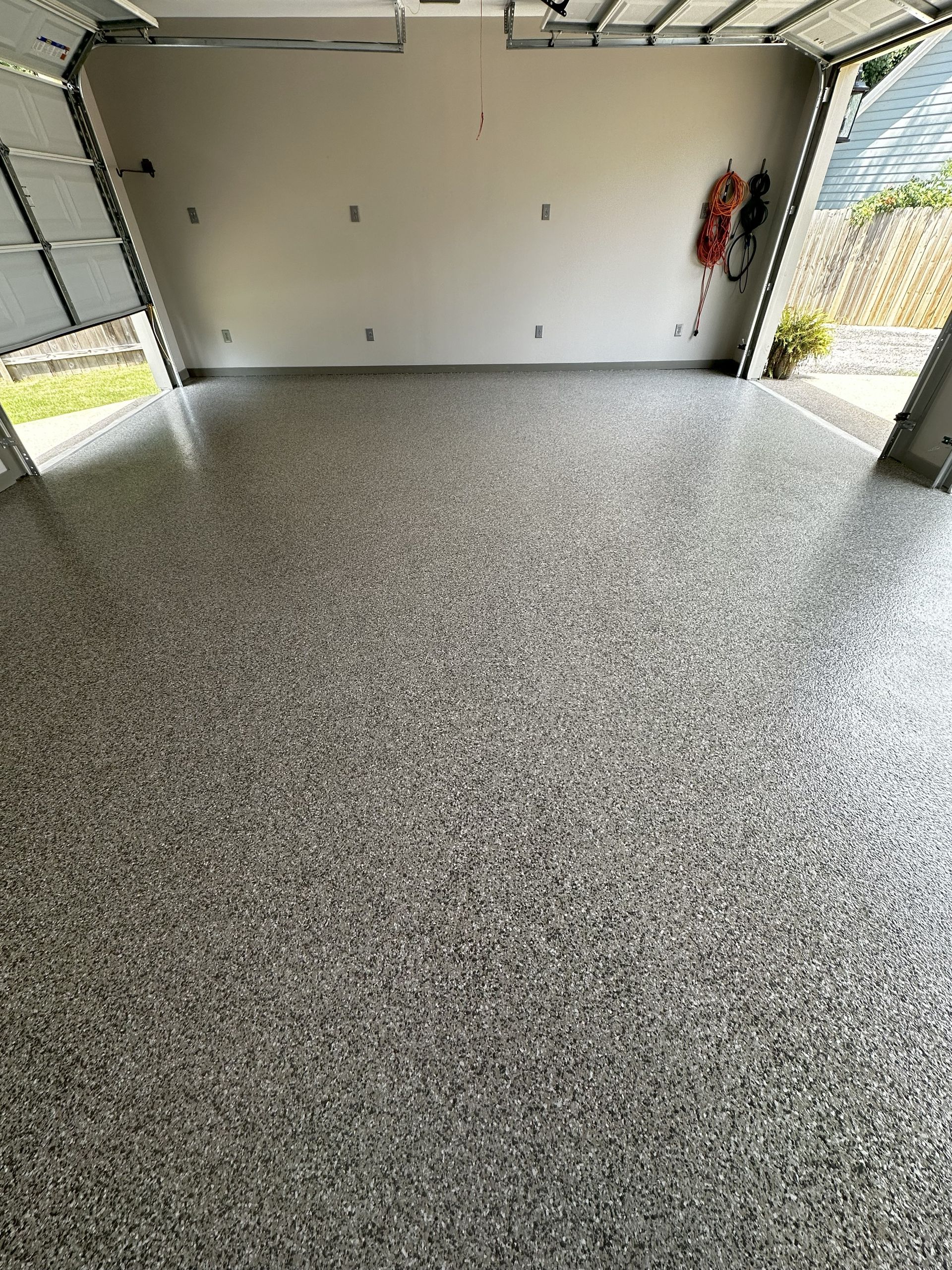 Garage with speckled gray epoxy flooring, white walls, and open garage door.