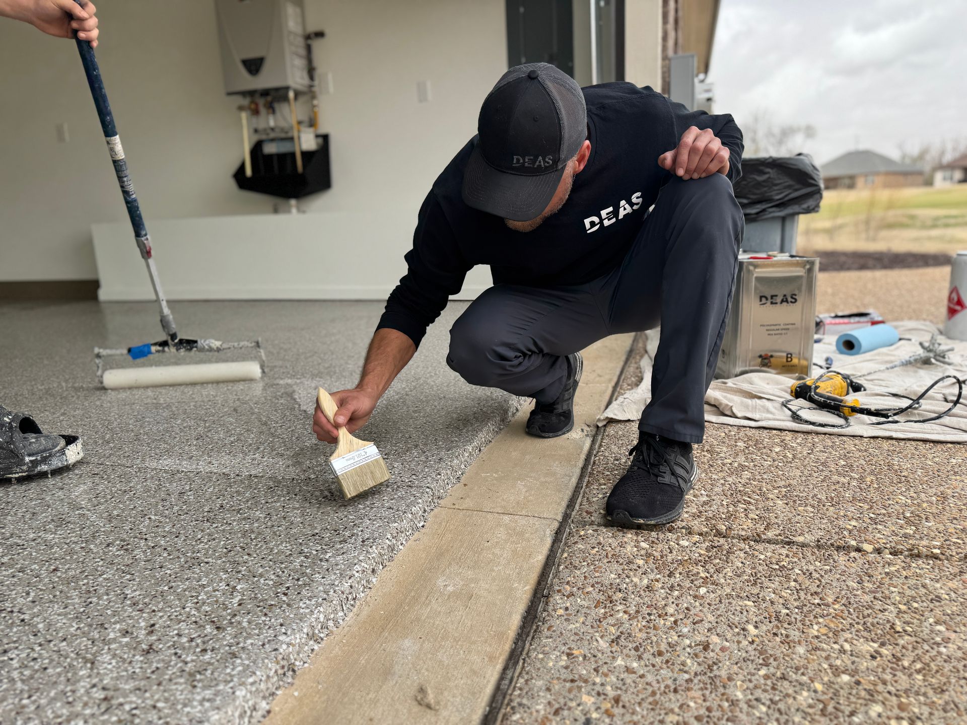 Worker kneeling on gravel rooftop, painting a seam with a small brush.