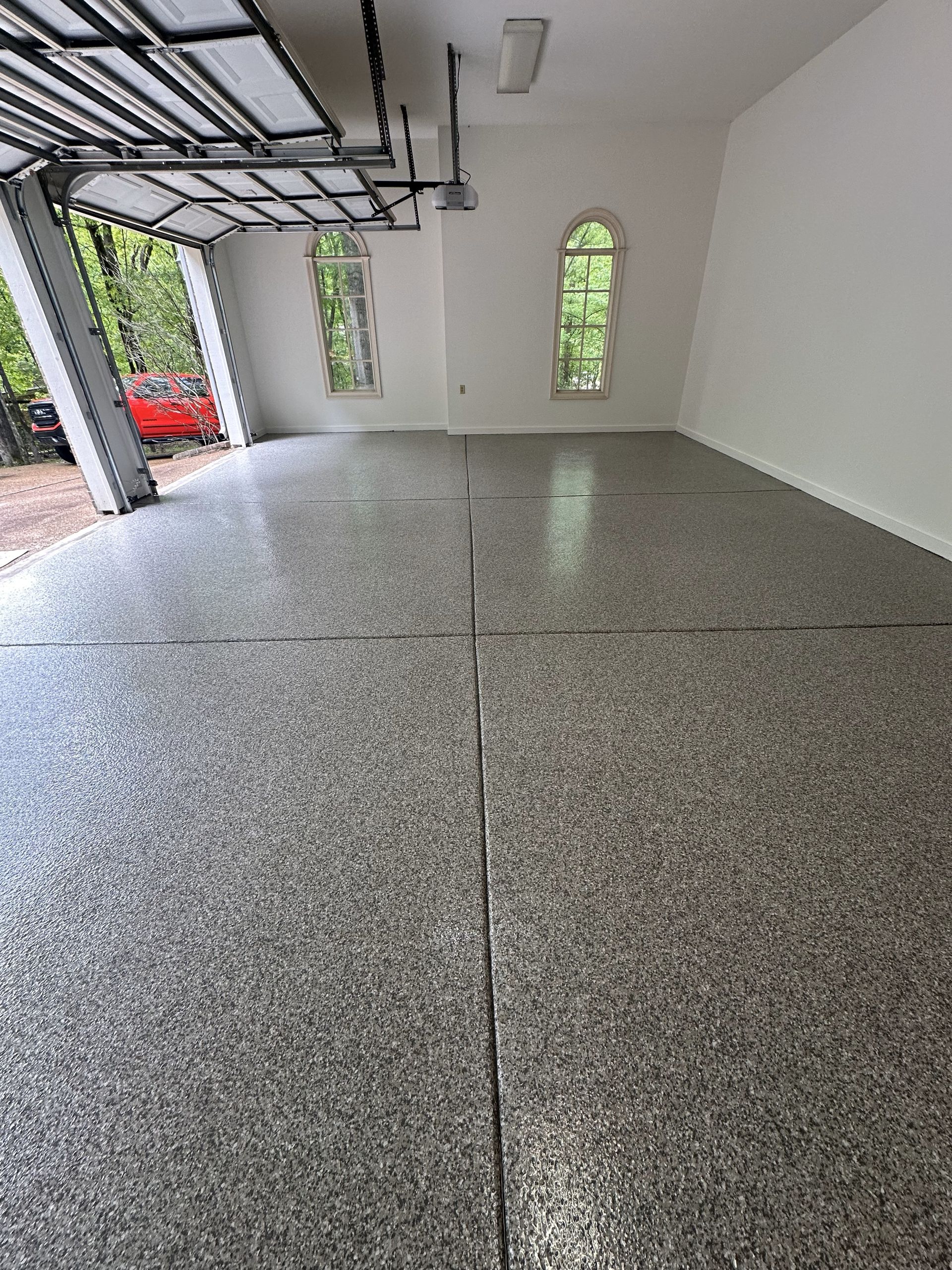 A garage with a gray floor and a red car parked in it.