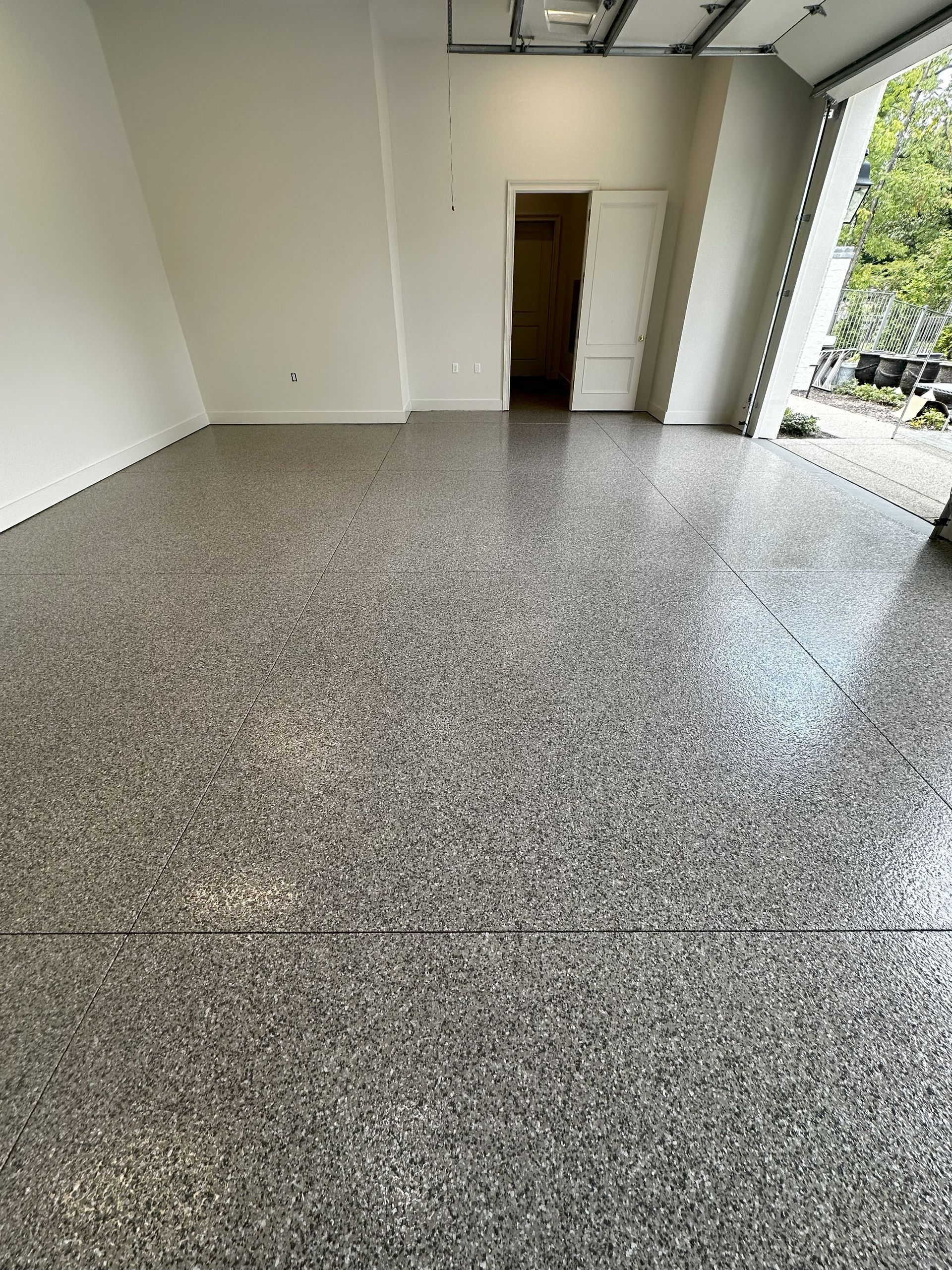 Interior view of a room with polished, speckled gray floor, white walls, and an open garage door.